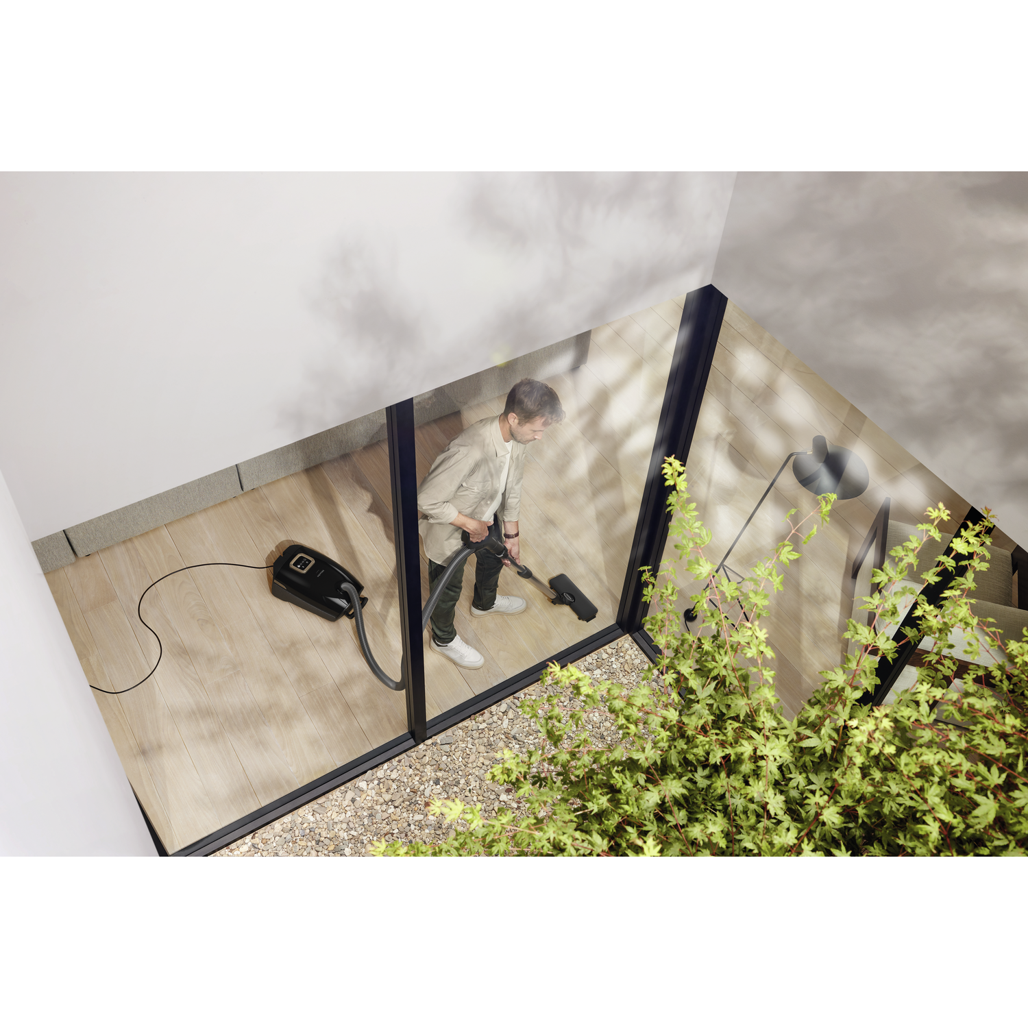 A person vacuuming a wooden floor, viewed from above, through a window.