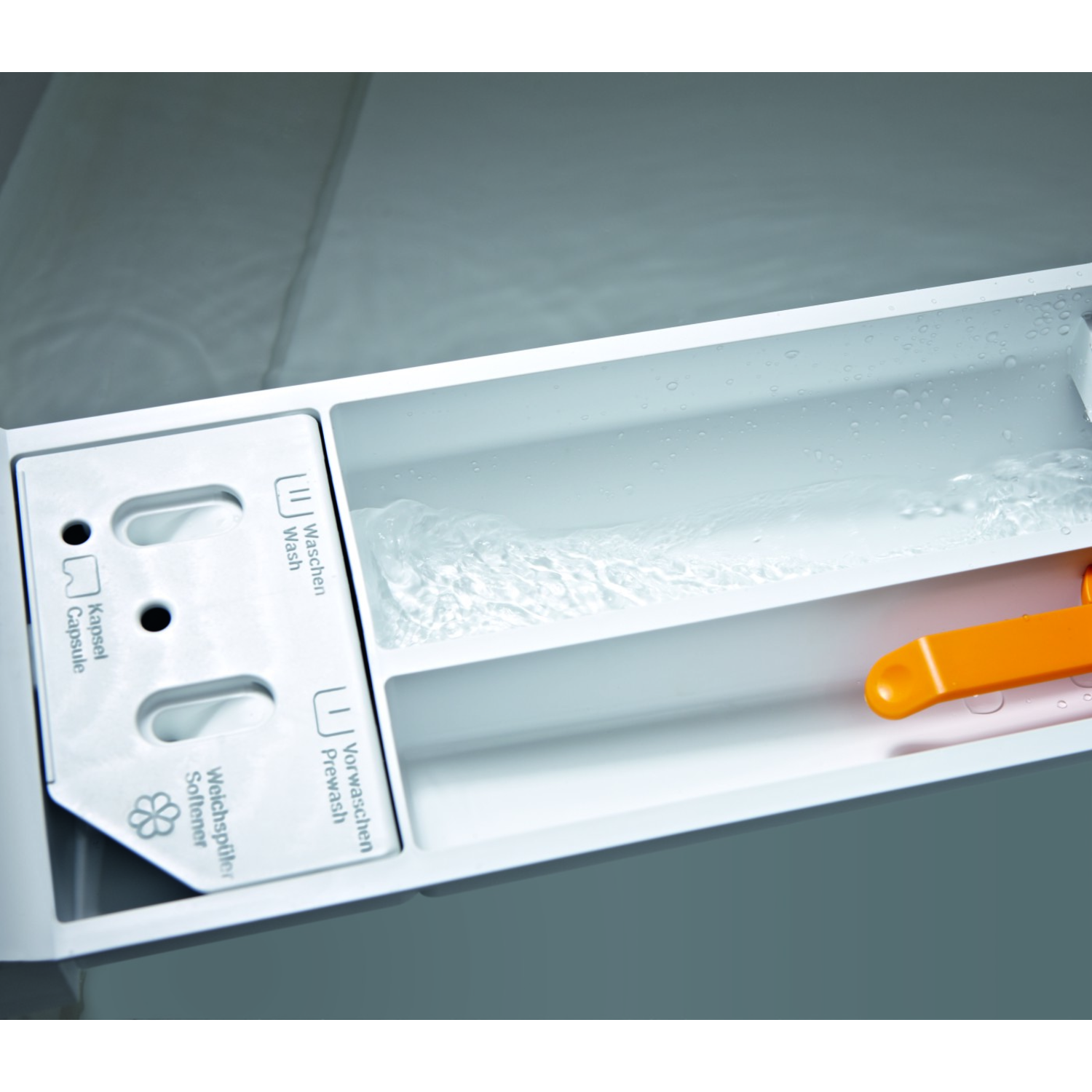 Washing machine detergent drawer filling with water. Orange dispenser visible, with compartments.