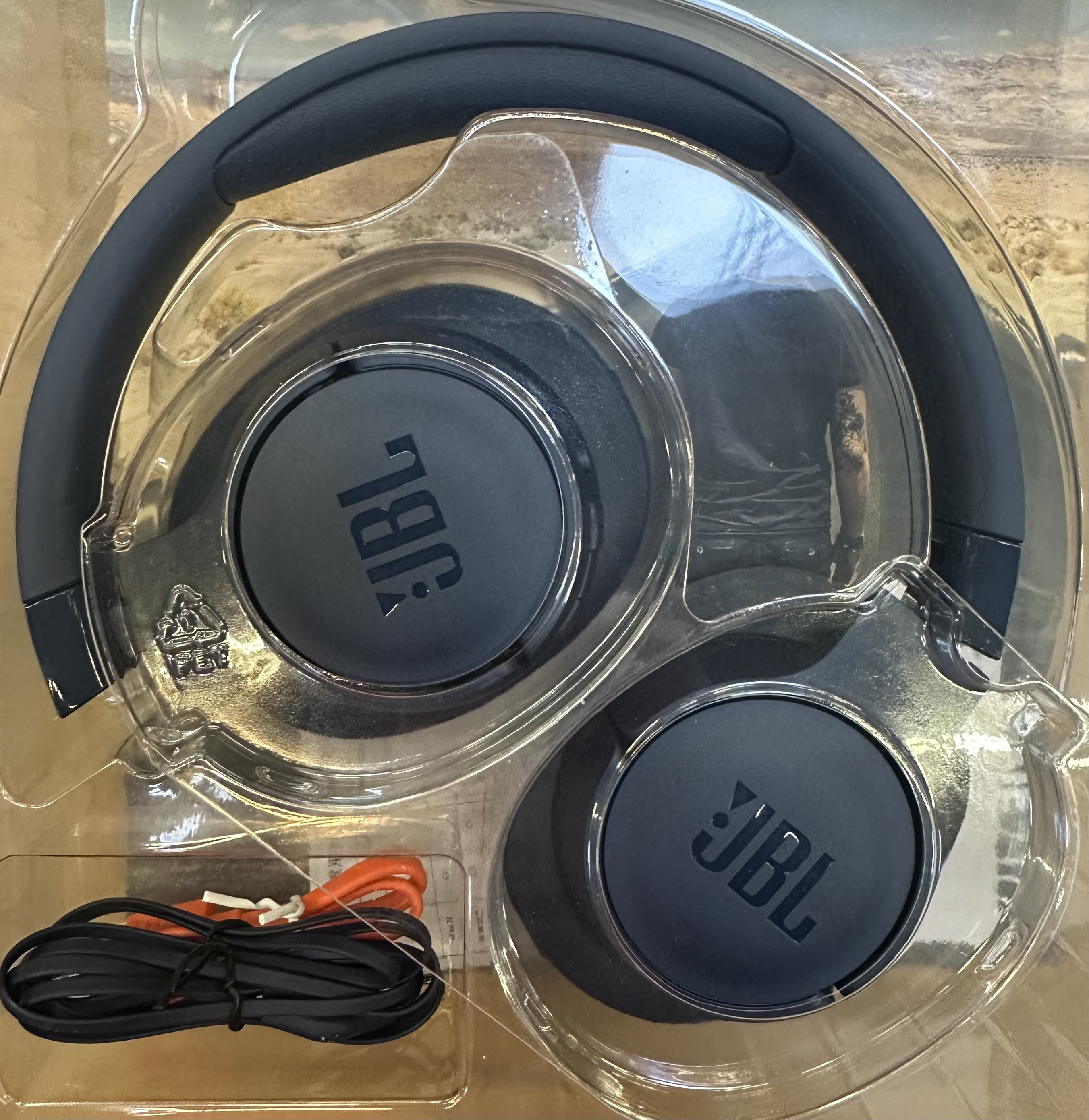 Czarne słuchawki JBL w przezroczystym plastikowym etui z pomarańczowym przewodem.