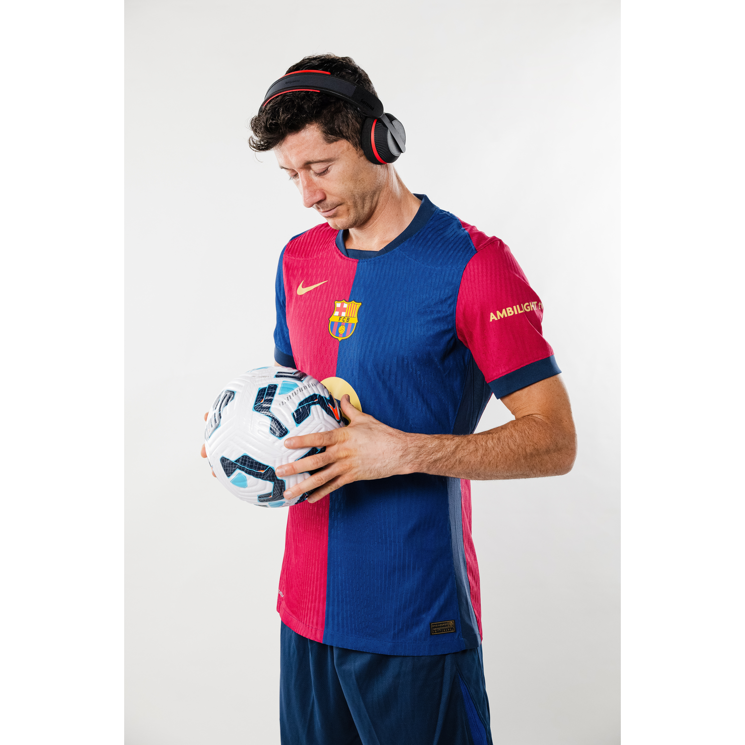 Een man in een Barcelona-shirt houdt een voetbal vast en draagt een zwart-rode koptelefoon.