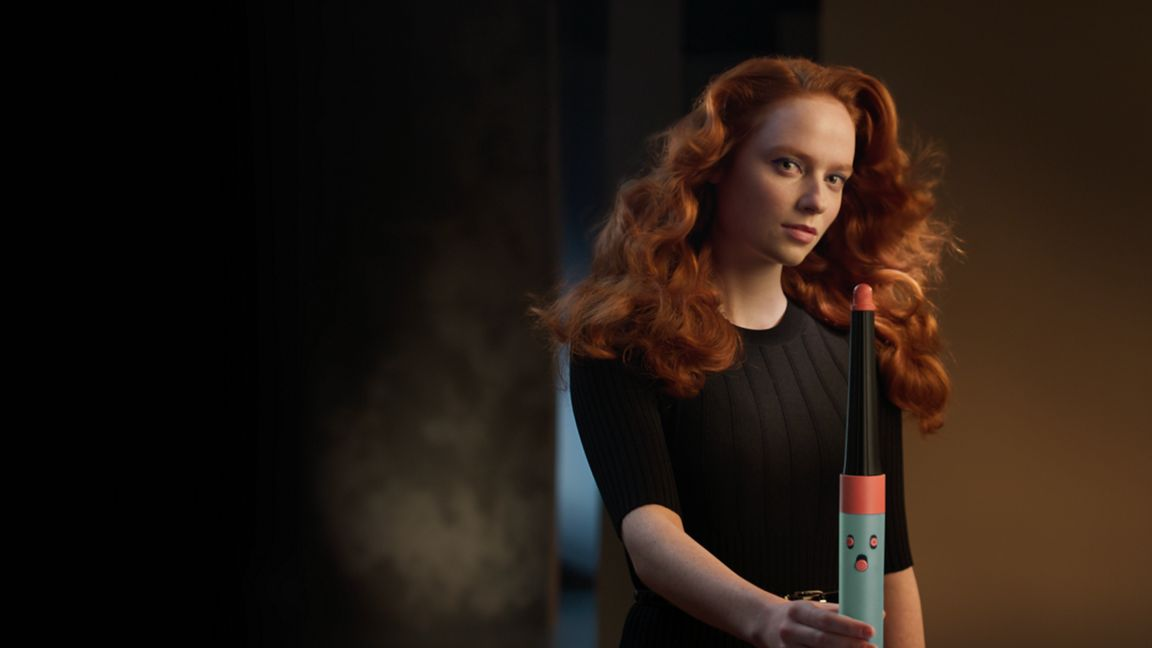 Donna dai capelli rossi che tiene in mano un ferro arricciacapelli con un volto di cartone animato.