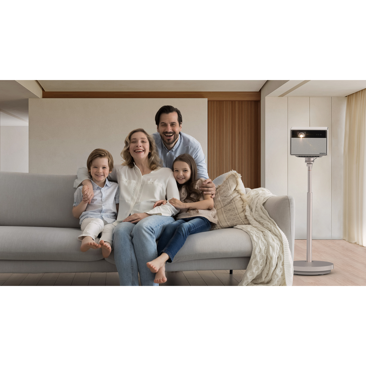 Une famille avec deux enfants sourit près d'un projecteur sur un pied. Canapé en arrière-plan.