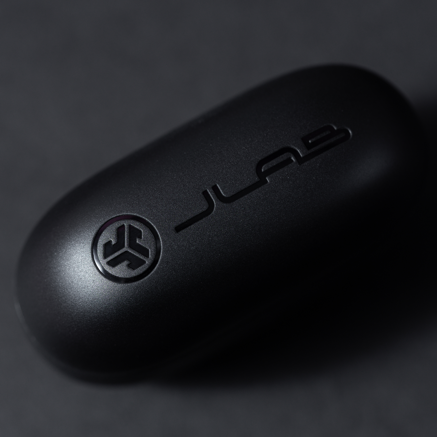 A black earbud case with the JLab logo. It is oval and matte black on a dark background.
