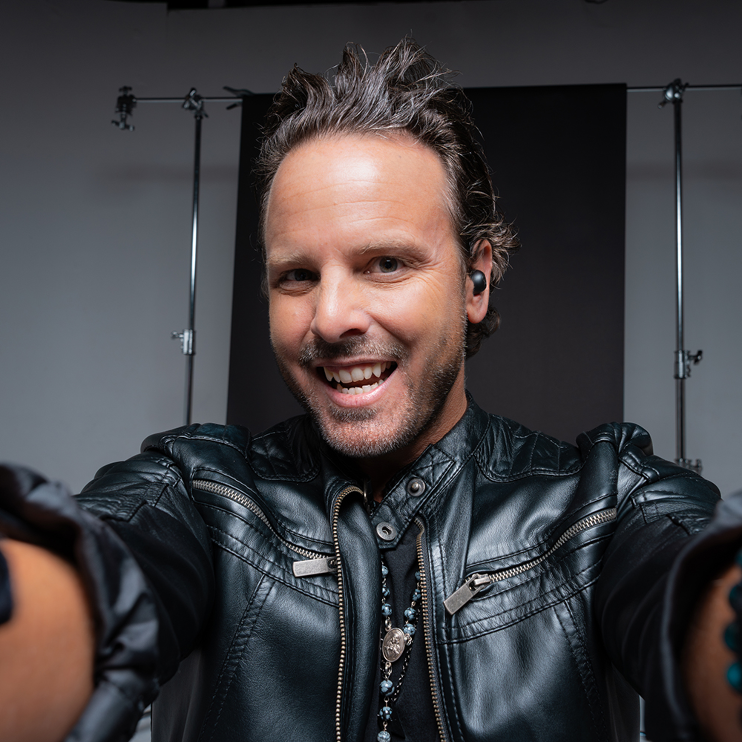 Man smiling, wearing earbuds. Black leather jacket, selfie.