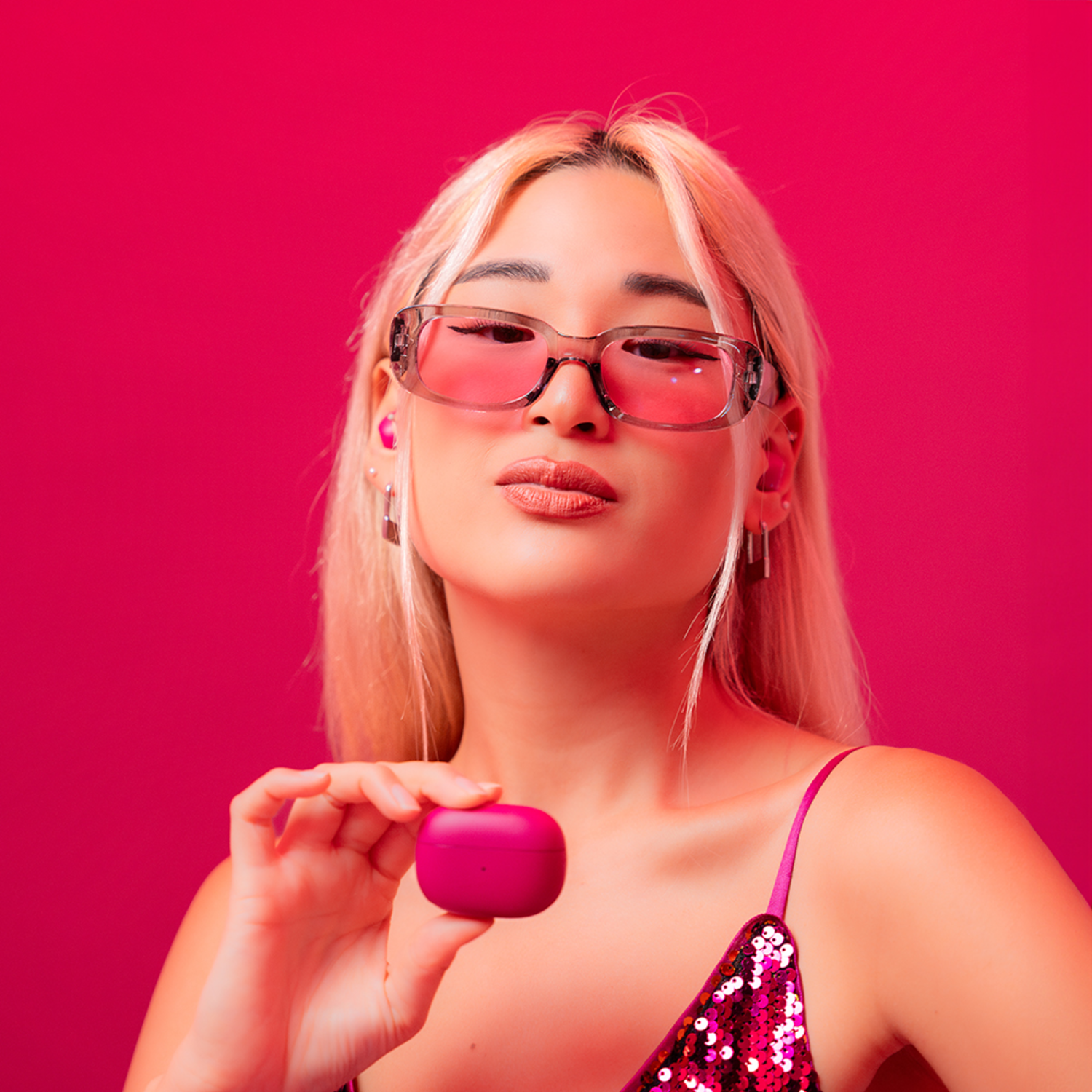 Woman in pink top holding a pink earbuds case, wearing glasses.