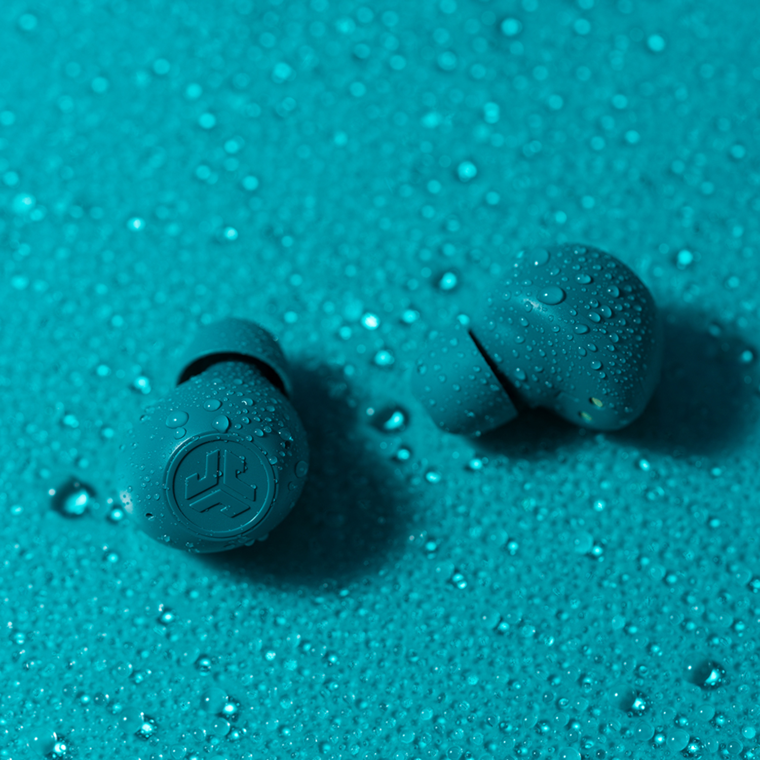 Twee blauwe oordopjes met waterdruppels op een blauw oppervlak.