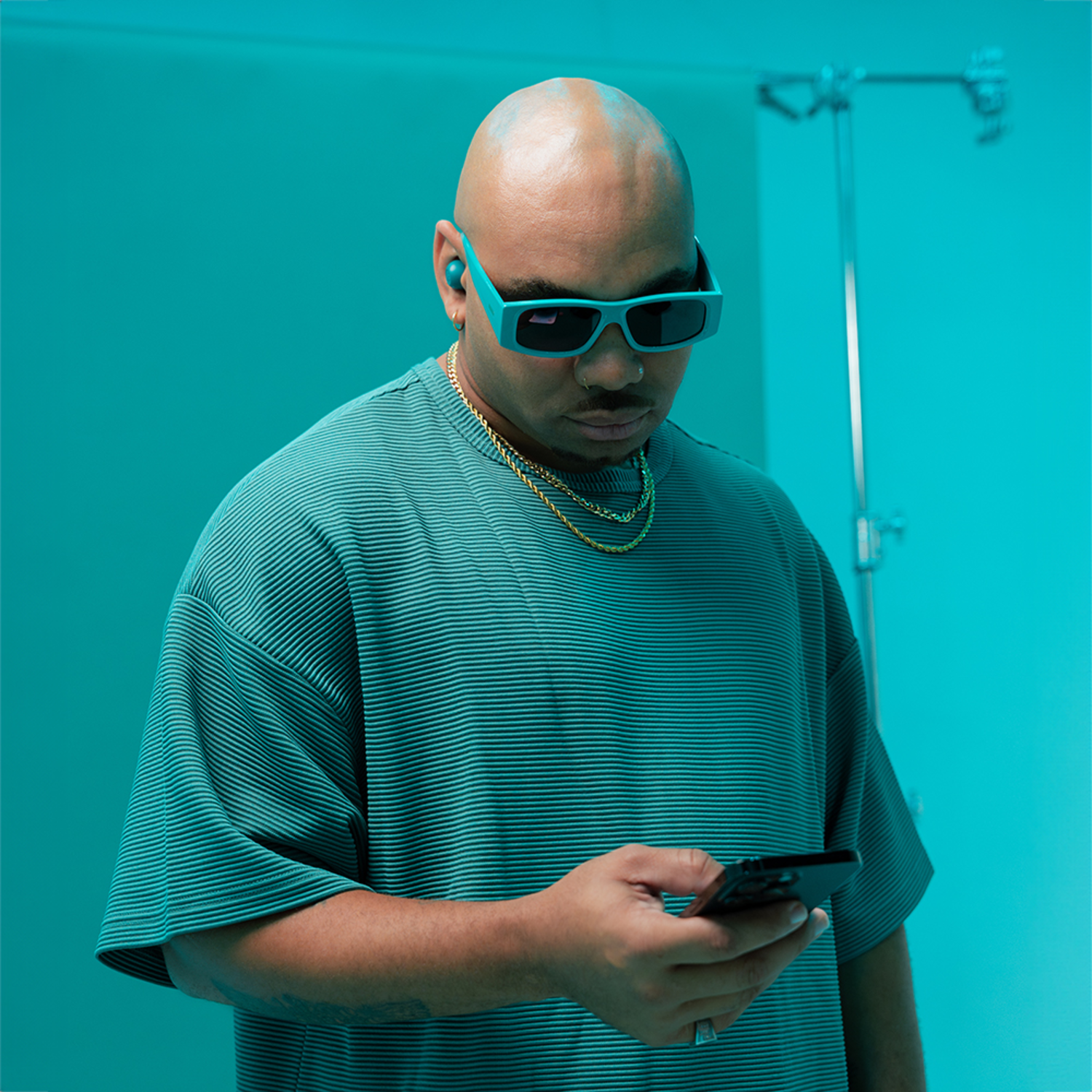 Kale man in een blauwgroene outfit die naar zijn telefoon kijkt.