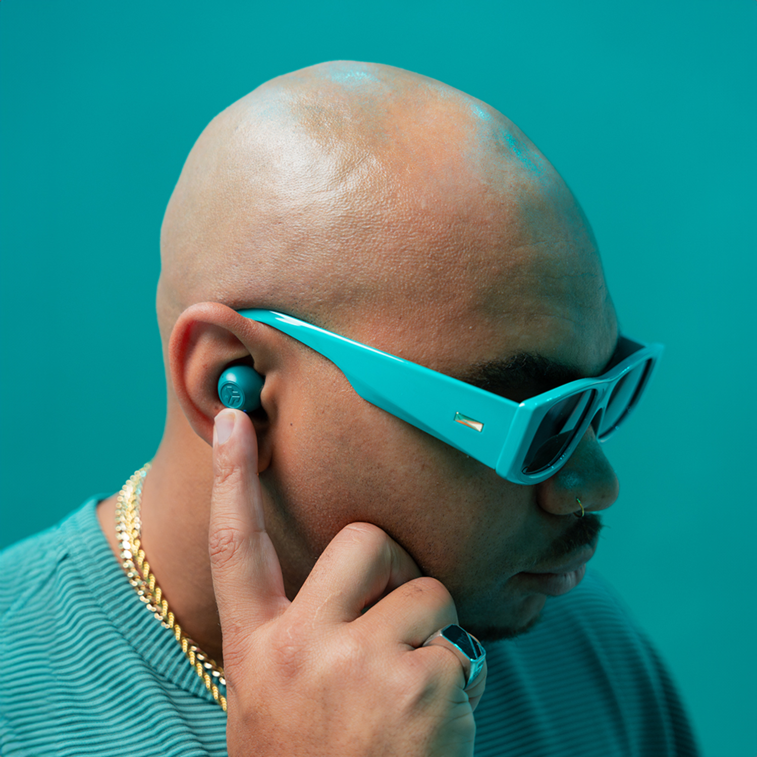Een man met turquoise zonnebril draagt een oortelefoon en gouden ketting. Turquoise achtergrond.