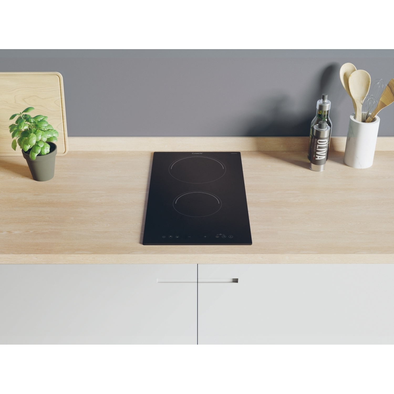 Piano cottura a induzione Candy nero su un piano di lavoro in legno. Ambiente cucina con piante, olio e utensili.