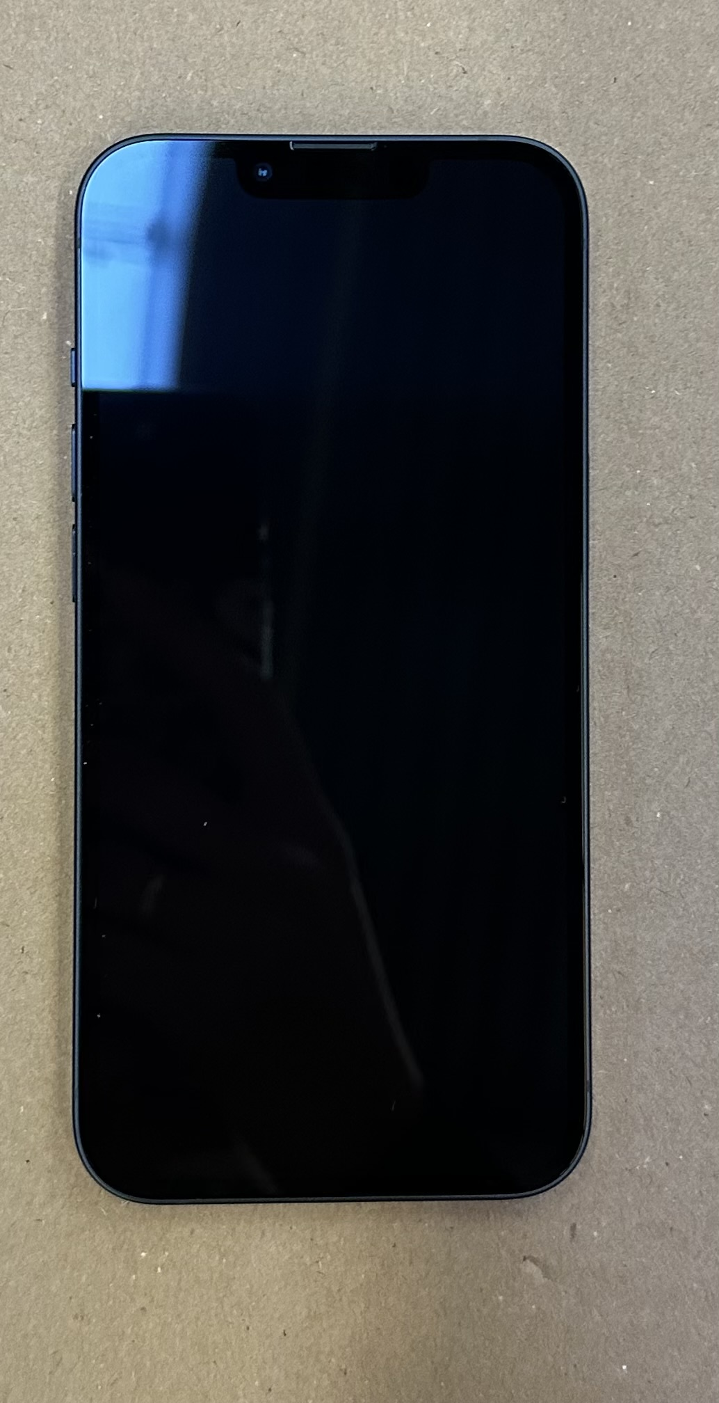 Ciemny smartfon leży na teksturowanej szarej powierzchni.