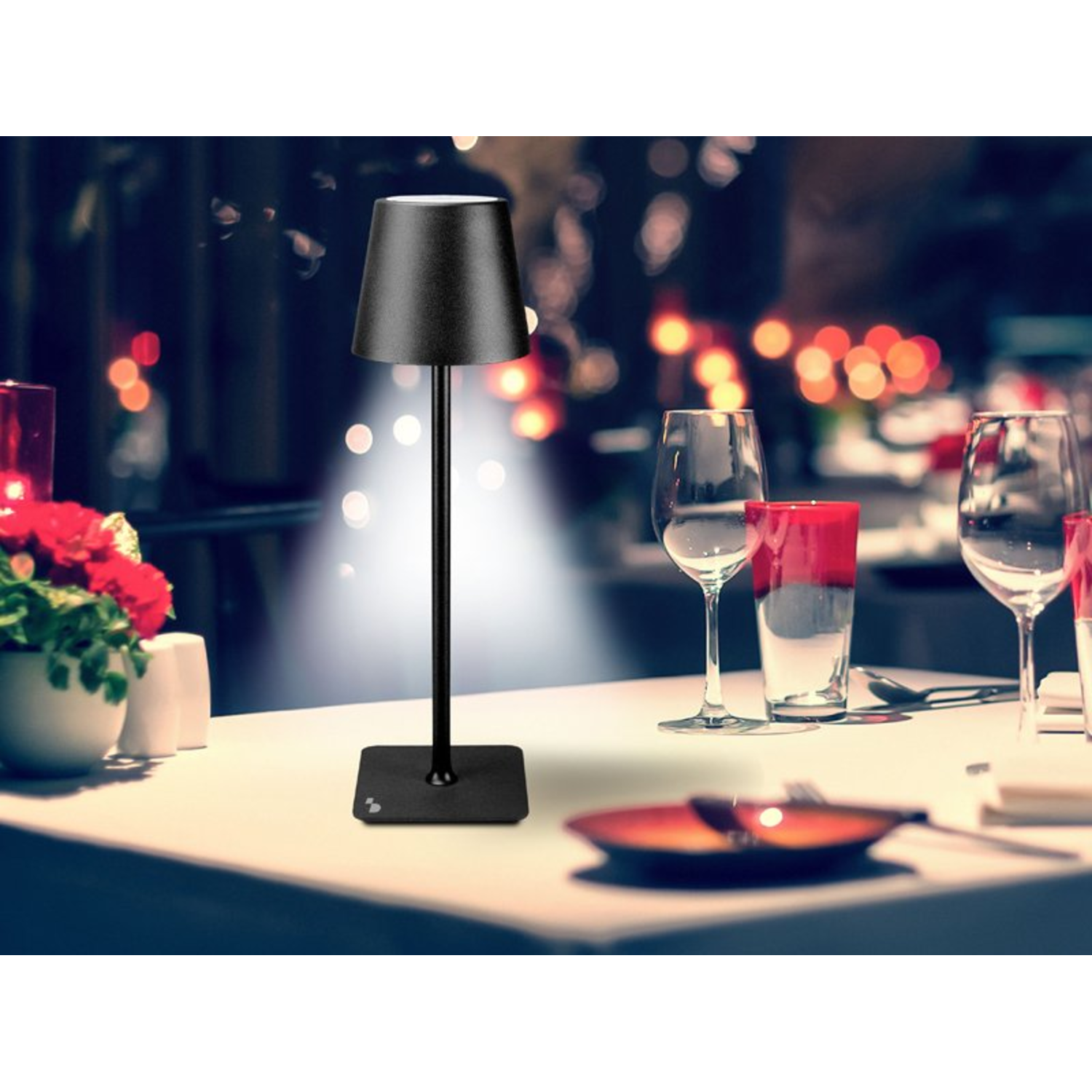 Zwarte aanraaklamp op een tafel. Wijnglazen en een rood bord staan ook op tafel in een kamer.