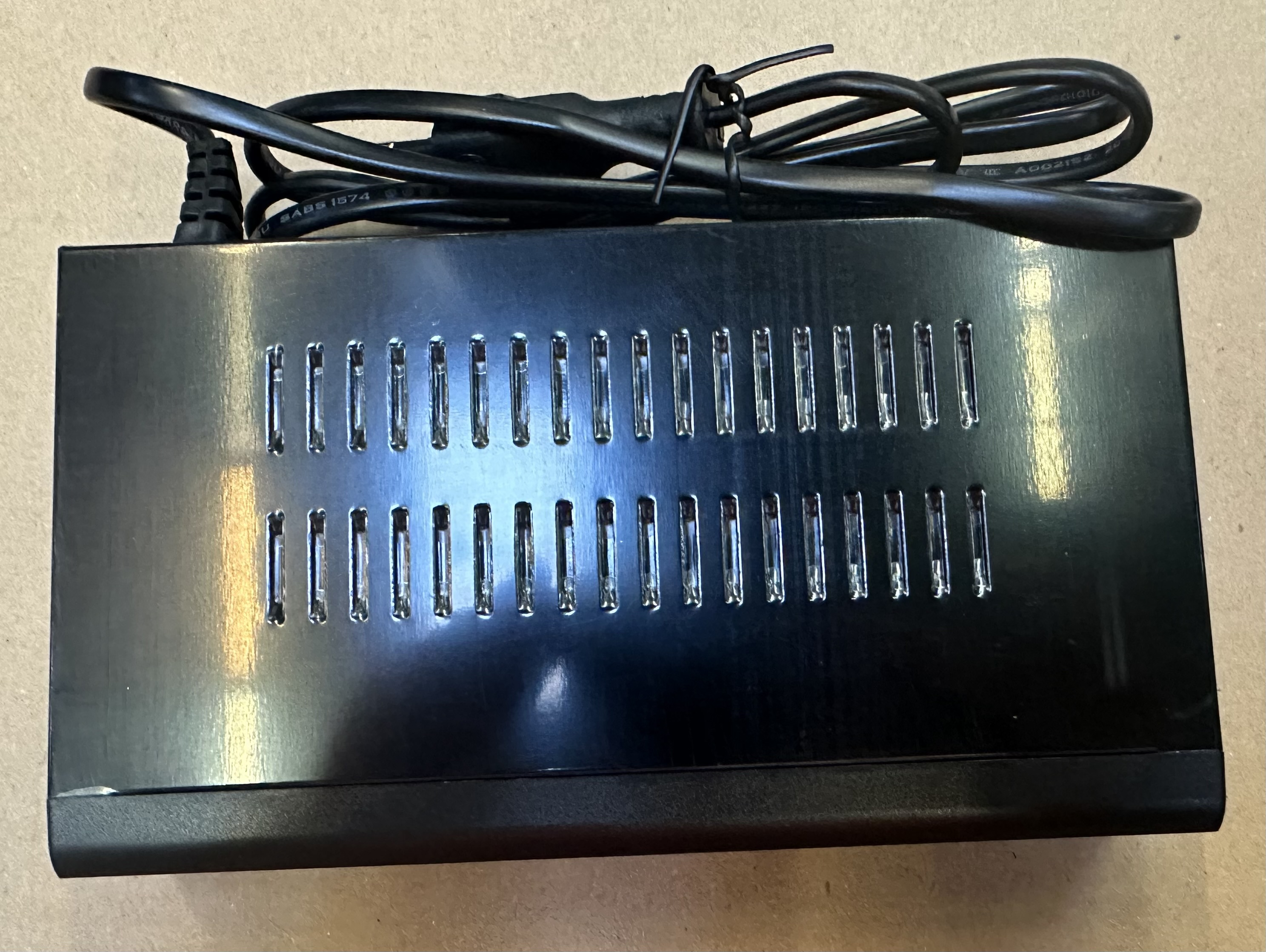 Czarny zasilacz z otworami wentylacyjnymi i czarnym przewodem zasilającym.