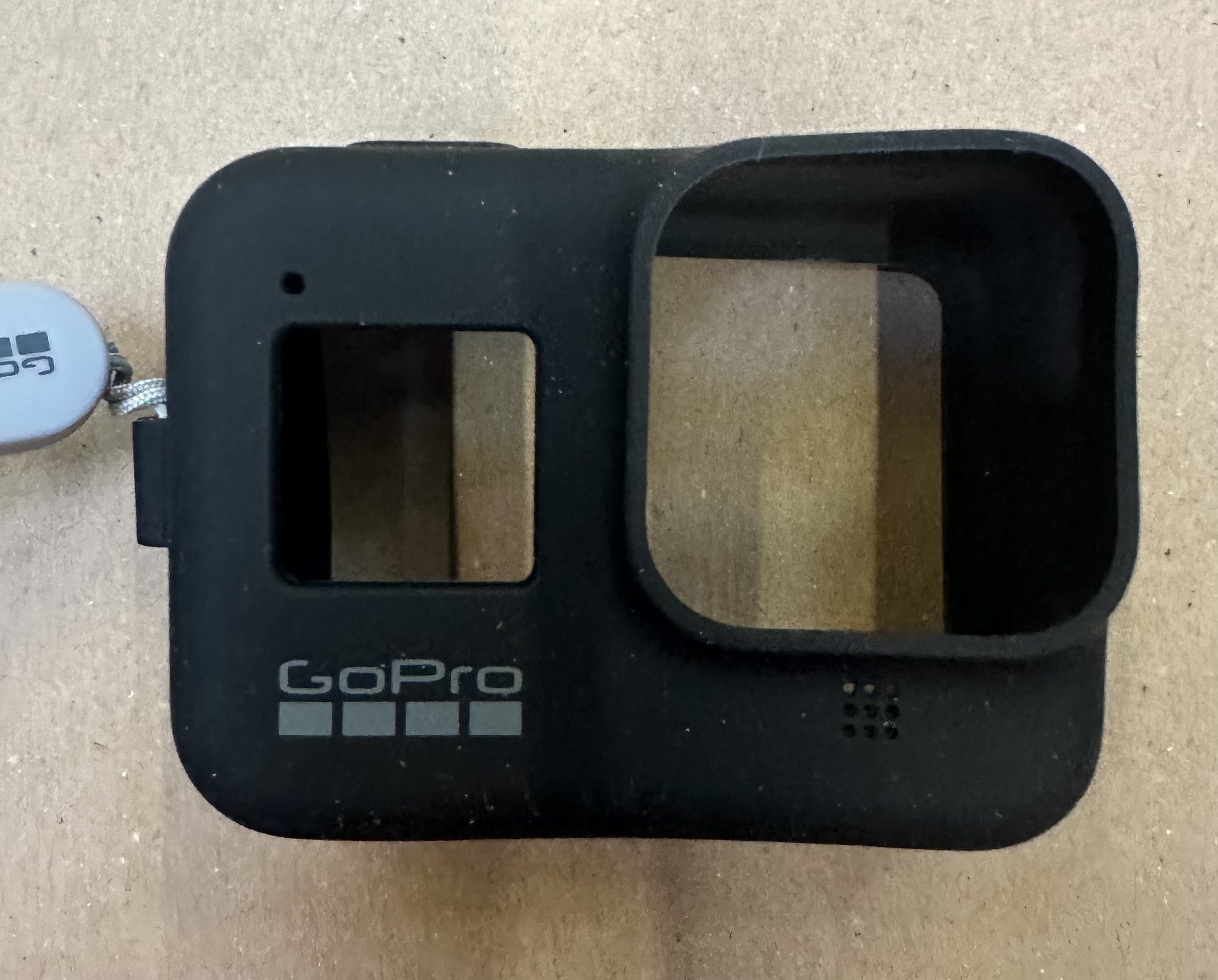 Czarny futerał na kamerę GoPro z logo GoPro i paskiem na nadgarstek. Ma otwory na obiektywy kamery.
