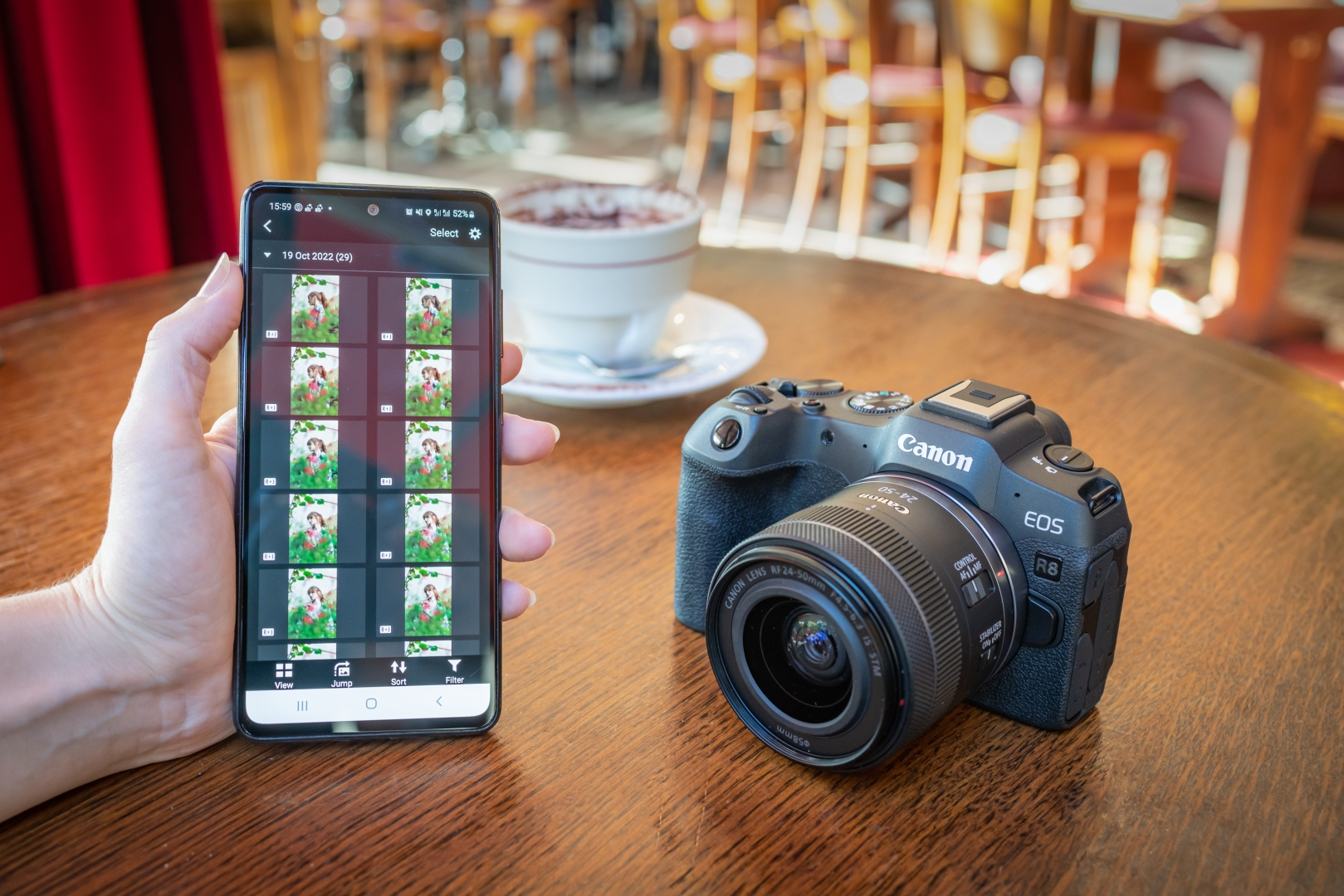 Eine Person hält ein Telefon mit Fotos, neben einer Canon Kamera auf einem Tisch.