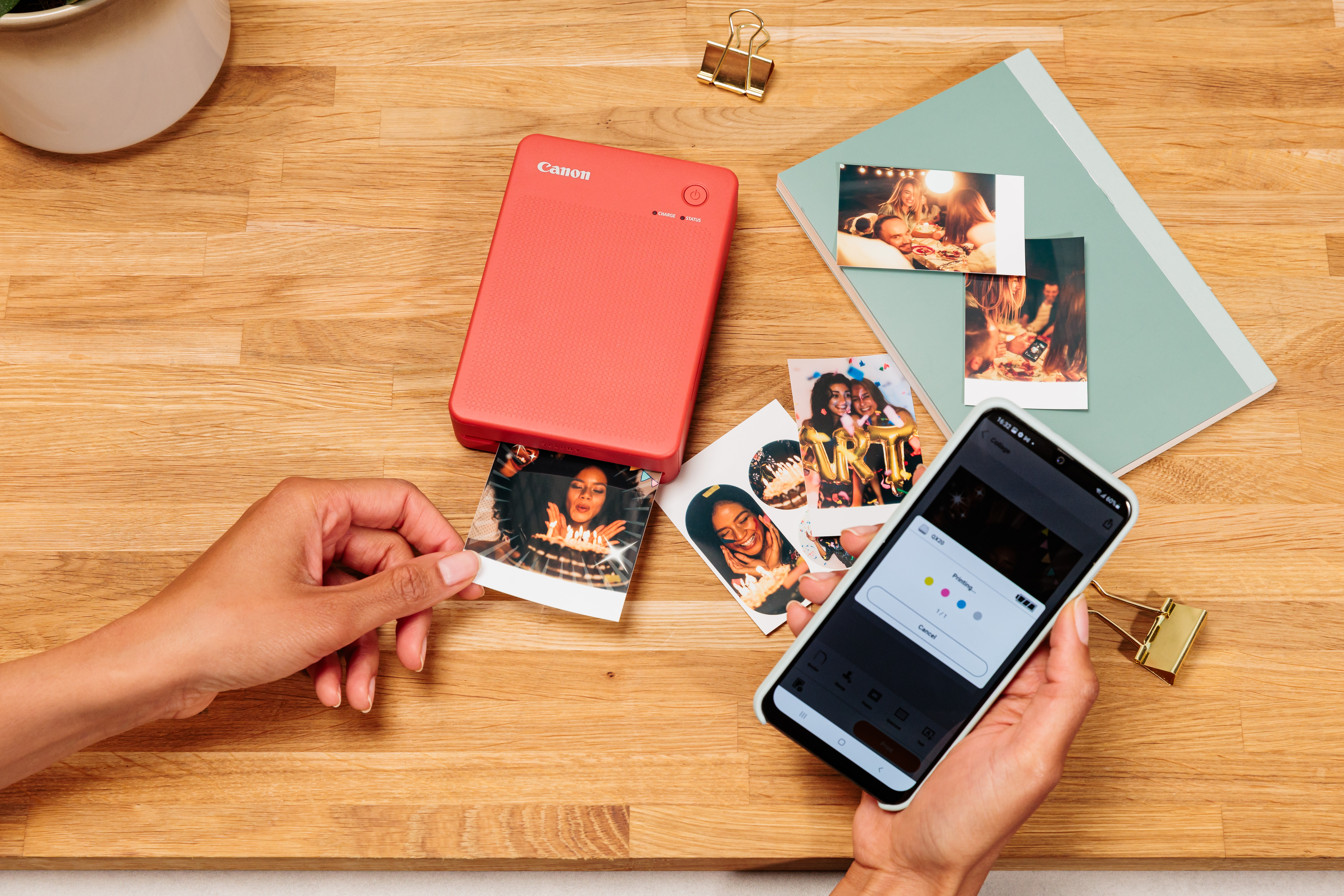 Eine Person druckt Fotos mit einem roten Drucker und einem Smartphone auf einem Holztisch.