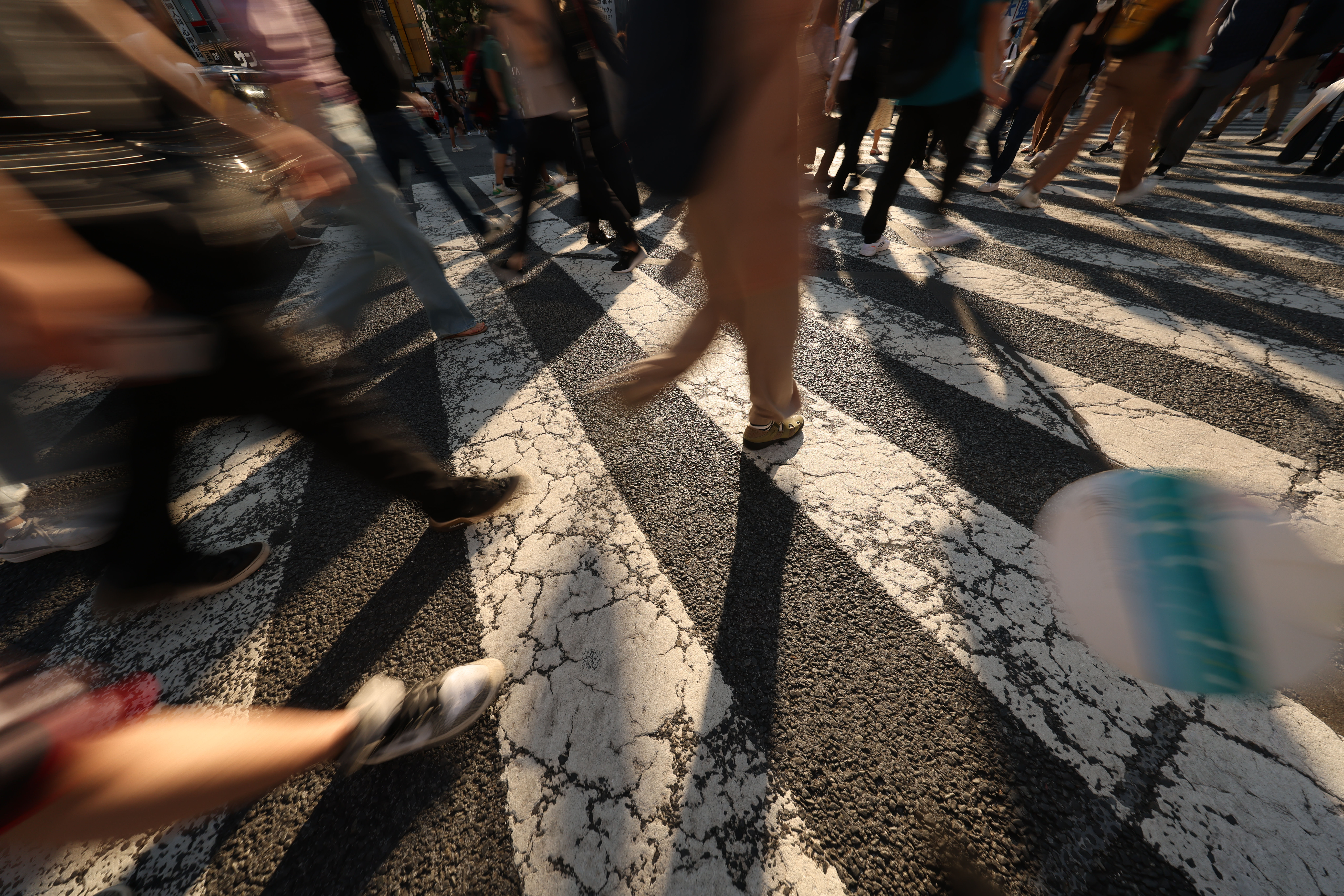Menschen überqueren eine Straße mit weißen Streifen und dunklem Asphalt. Bewegungsunschärfe.