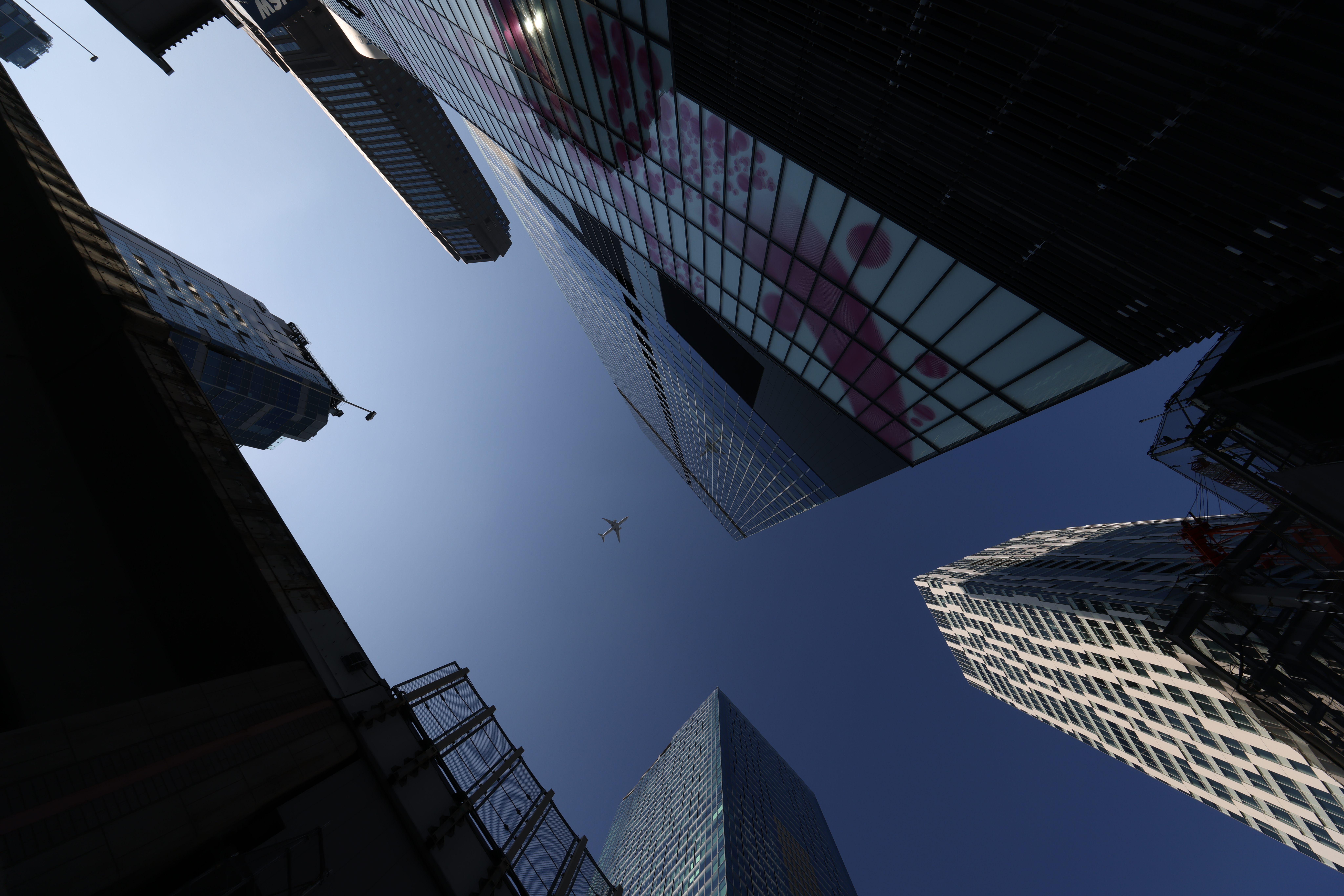 Gebäude, von unten gegen einen blauen Himmel mit einem Flugzeug in der Mitte aufgenommen.