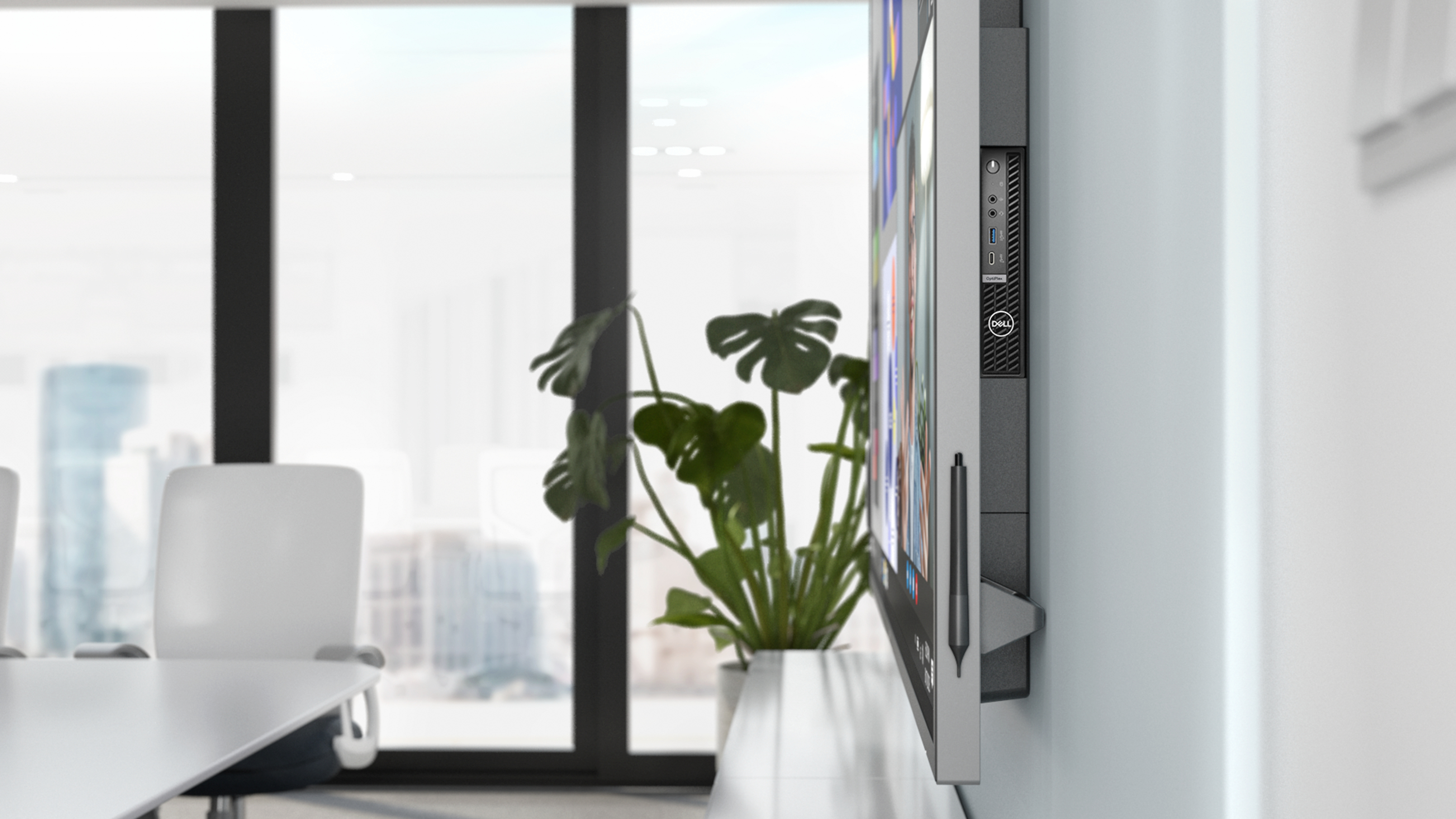 Ein Computer ist an einer Wand montiert. Eine Pflanze und Stühle befinden sich im Hintergrund eines Besprechungsraums.