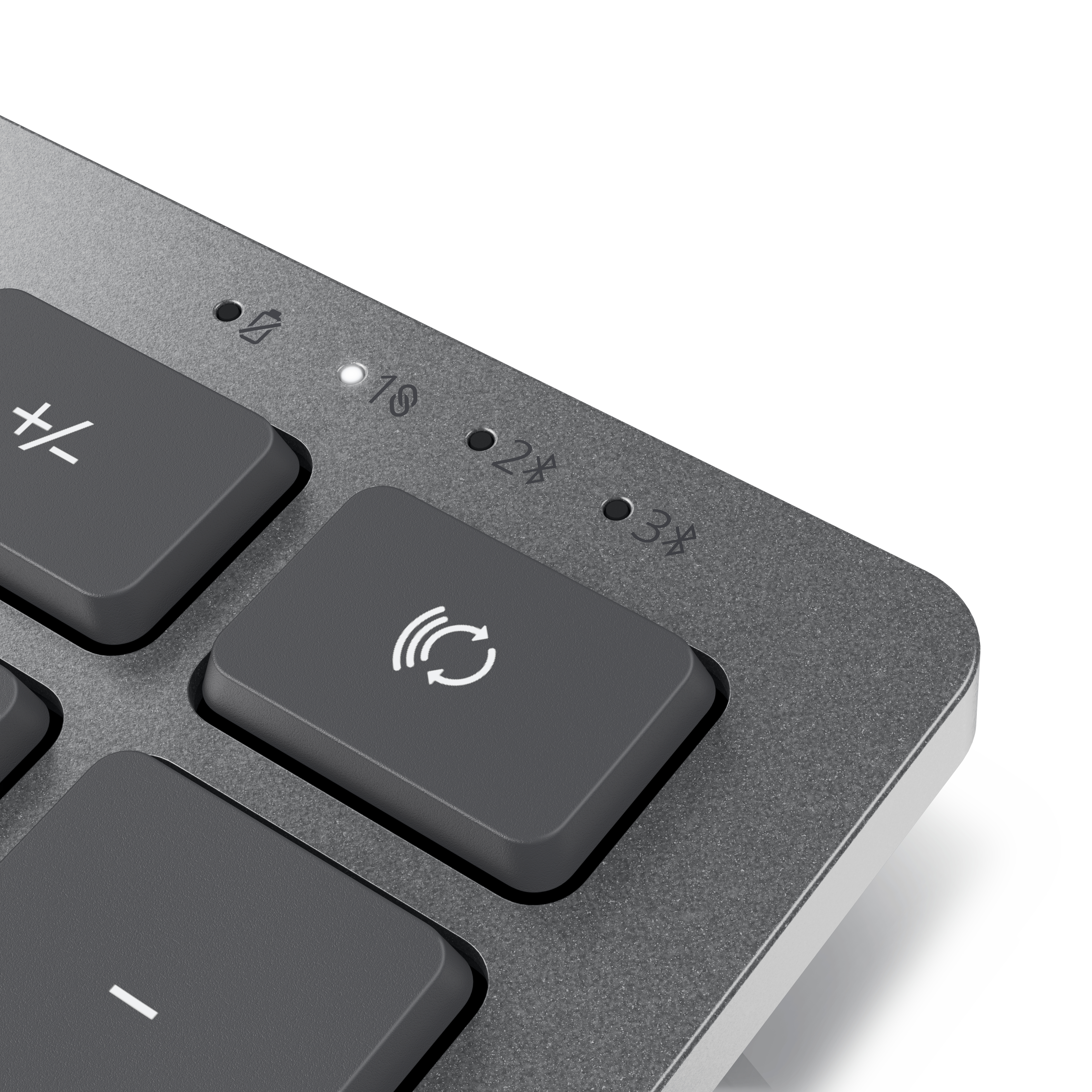 Primer plano de un teclado gris. Los botones incluyen: +/- y un símbolo inalámbrico. Luces LED encima de las teclas. Fondo blanco.