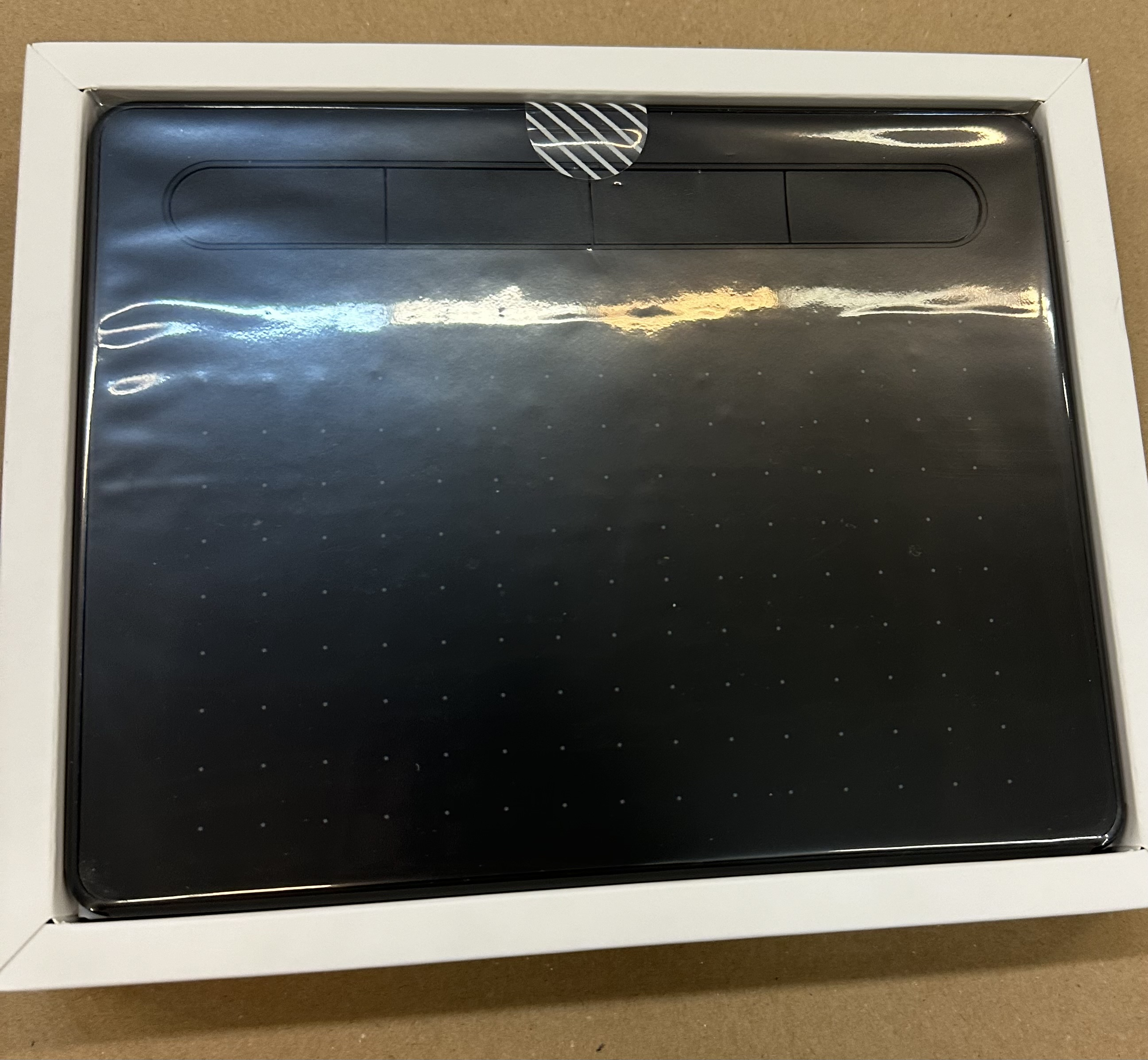 Czarny tablet do rysowania w białym pudełku, z przezroczystym plastikowym zamknięciem.