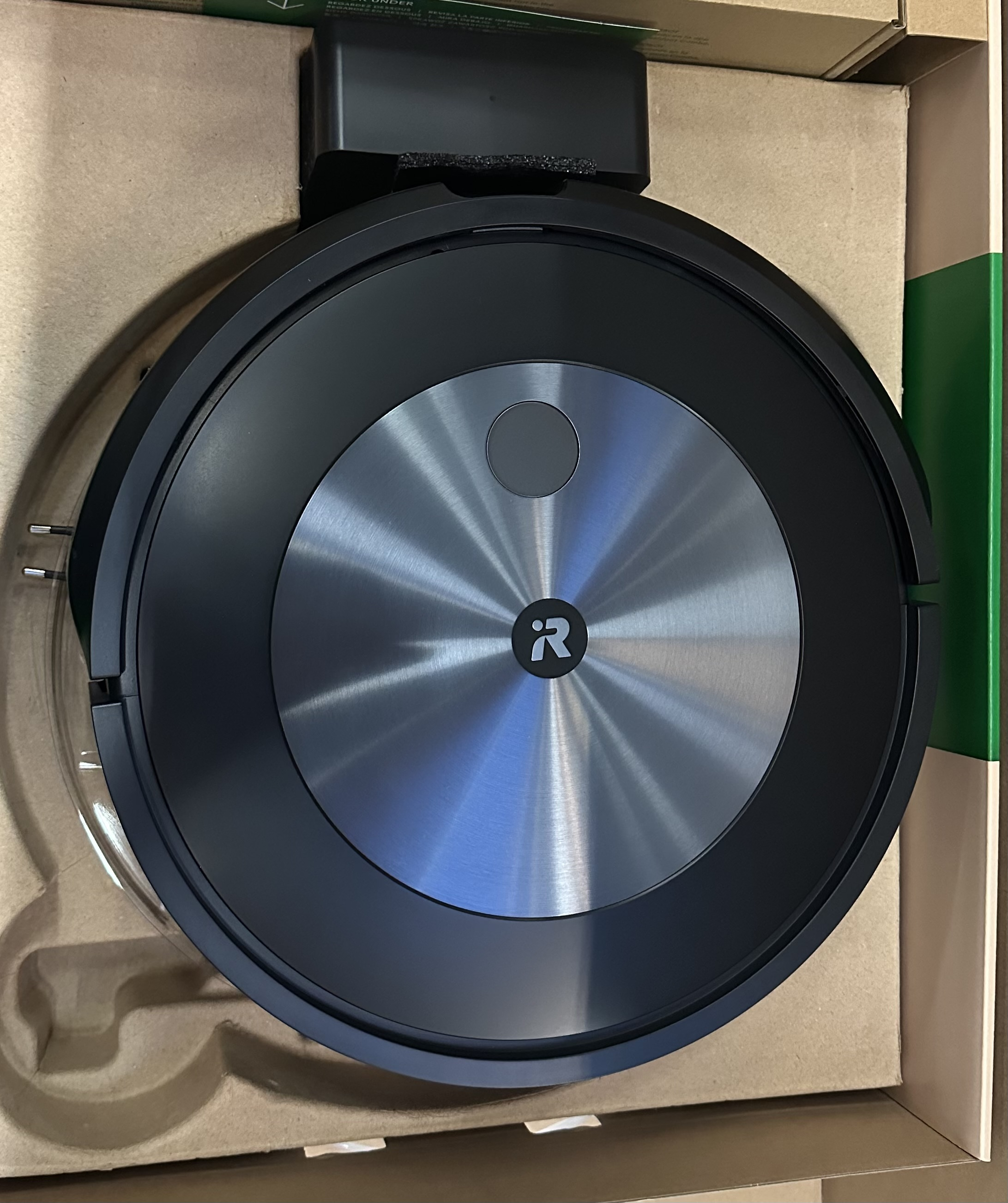 Czarny robot odkurzający Roomba w stacji ładującej, wewnątrz kartonu. Widok z góry.