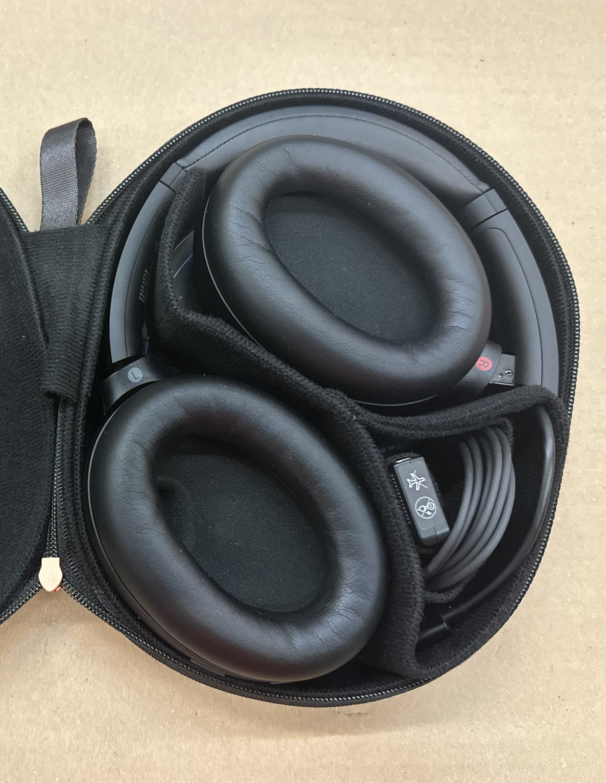 Czarne słuchawki z dużymi nausznicami w otwartym czarnym etui. Widoczny jest także kabel i USB.