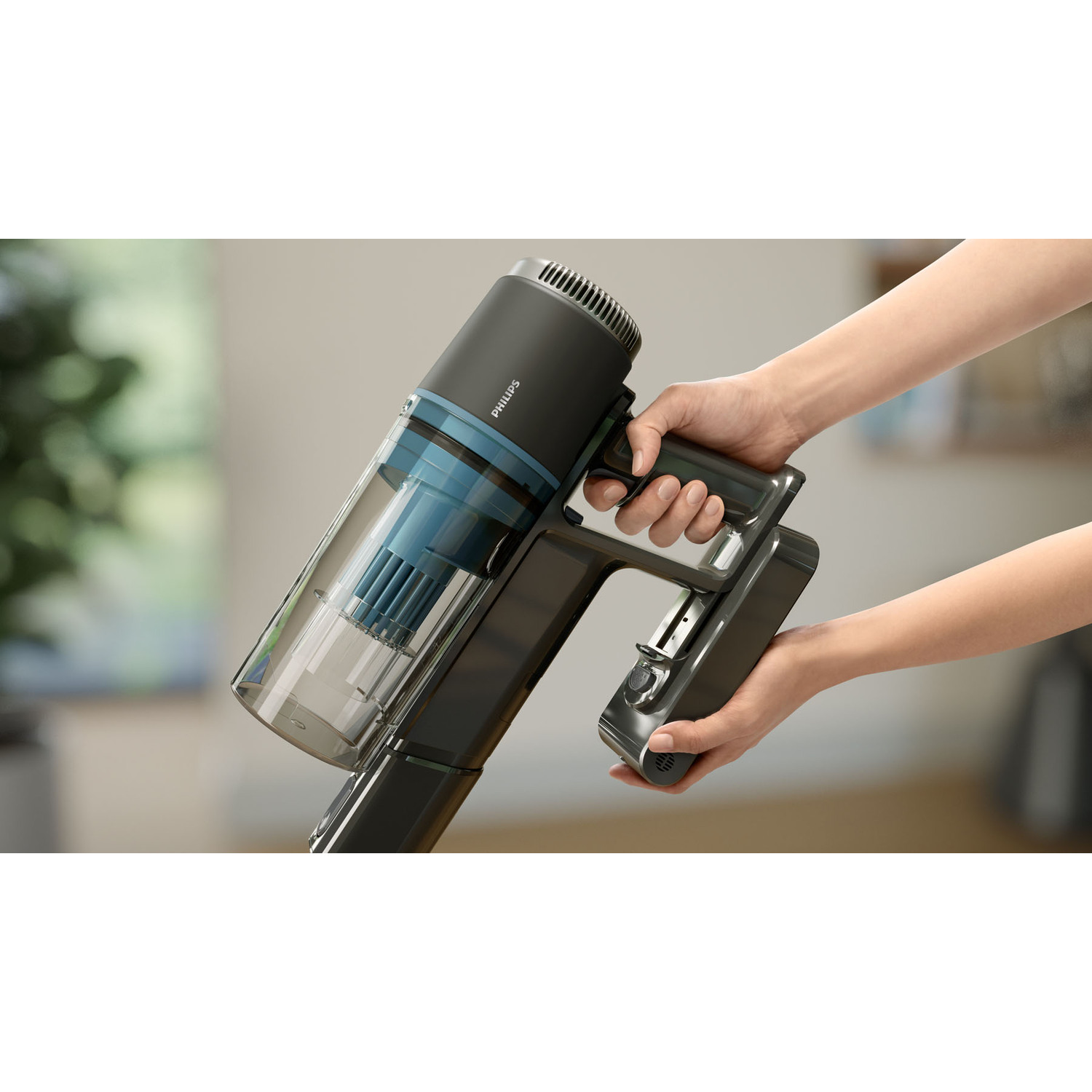 Hands holding a gray and black Philips vacuum cleaner, close-up view with blurred background.