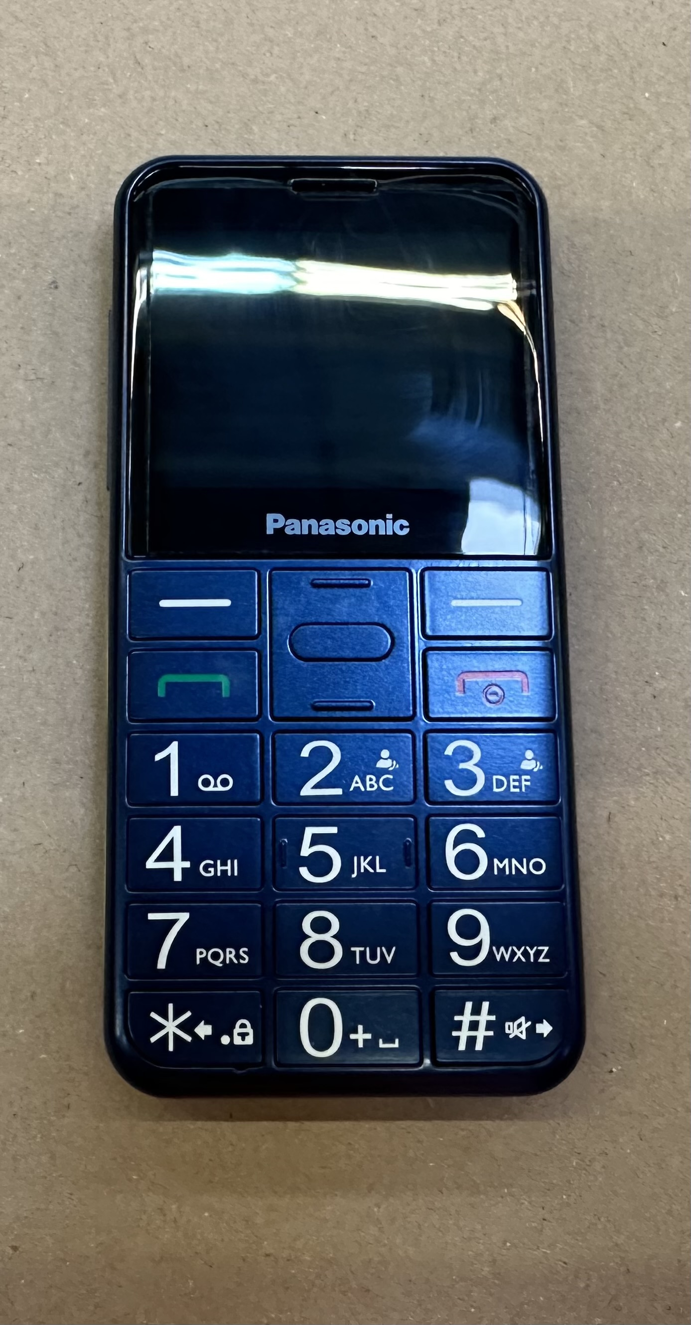 Niebieski telefon Panasonic z klawiszami numerycznymi i małym ekranem. U góry napis Panasonic.