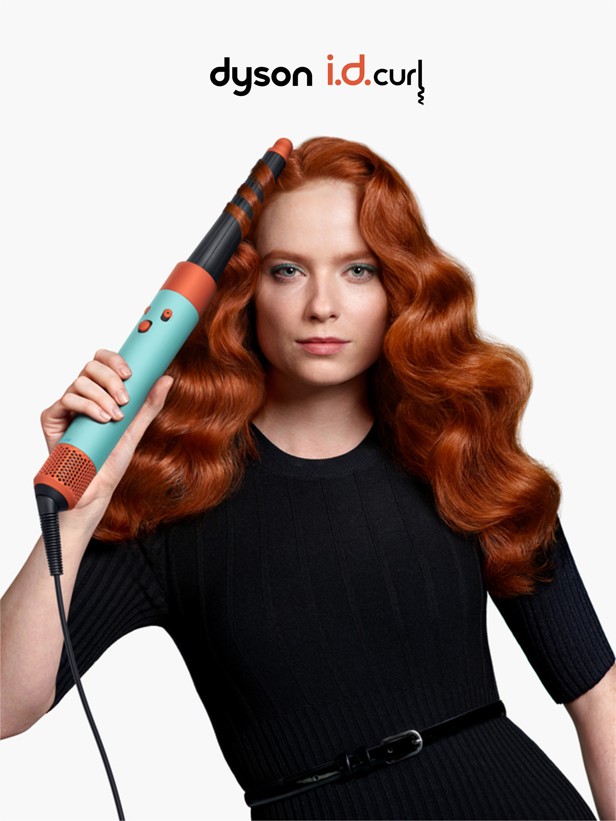 Una mujer sosteniendo un rizador de pelo turquesa, negro y naranja con cabello rojo y un vestido negro.