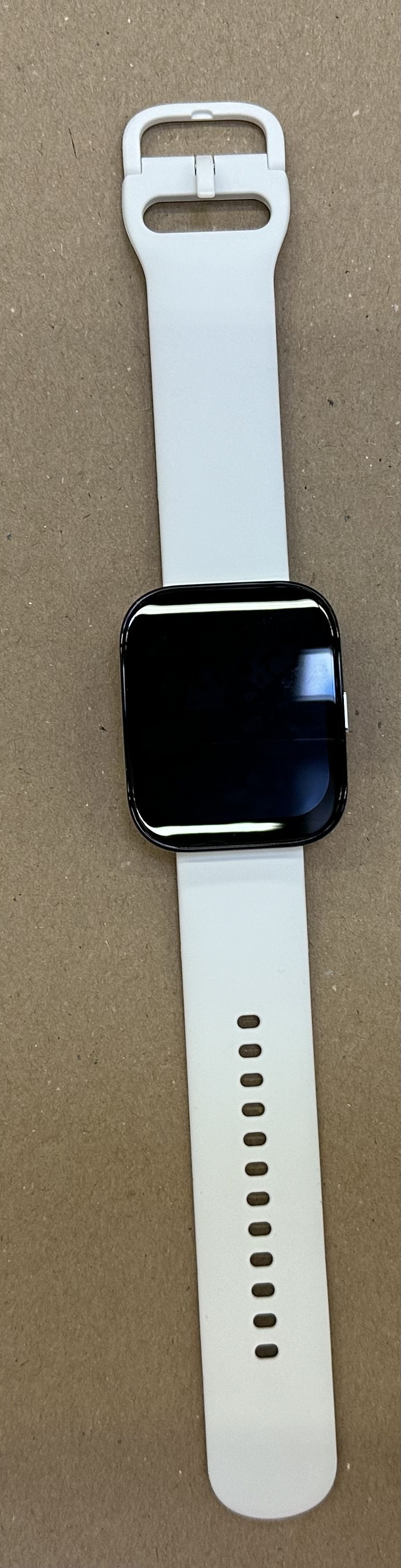 Smartwatch z czarnym ekranem i białym paskiem, leżący na powierzchni.