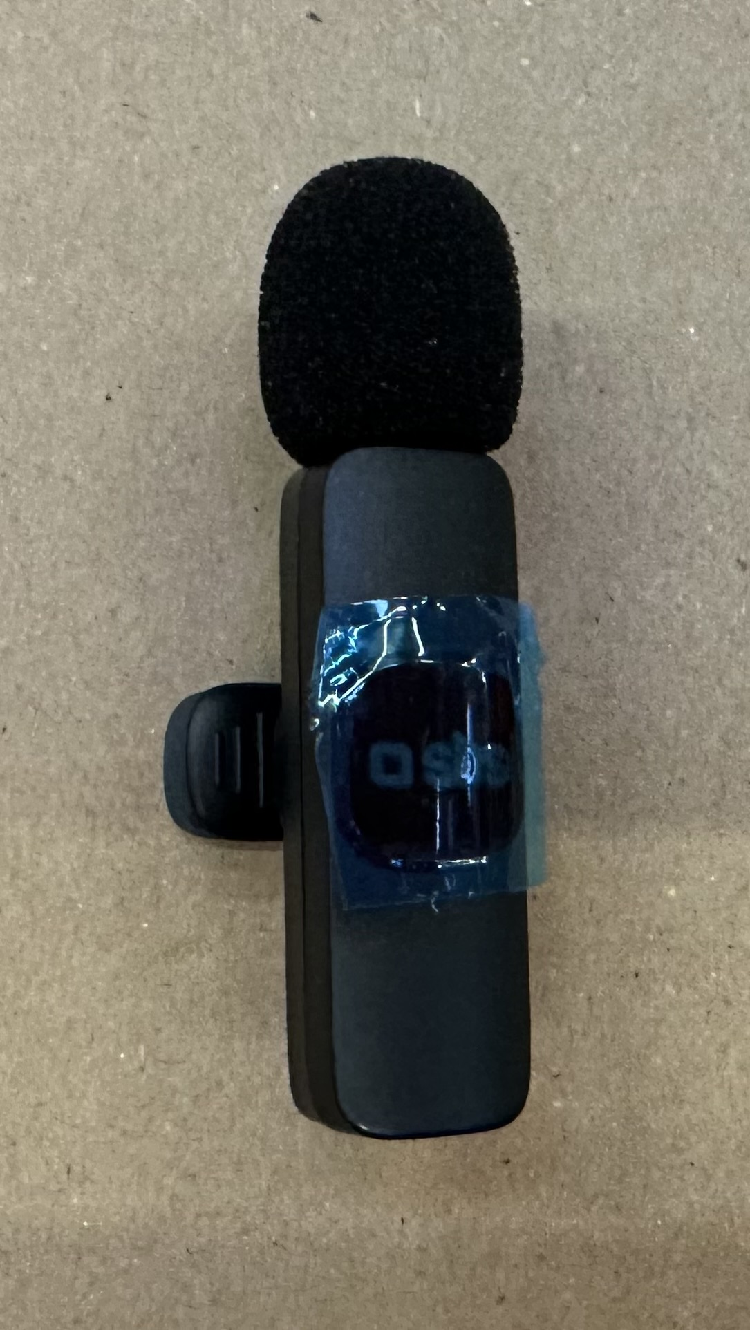 Czarny mikrofon na beżowej powierzchni. Mikrofon jest przymocowany do małego klipsa.