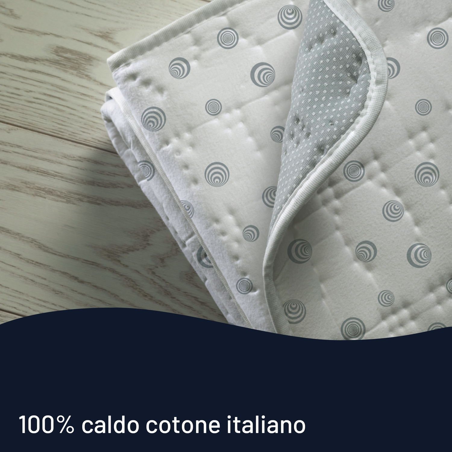 Coperta bianca piegata con cerchi grigi su un tavolo di legno. È visibile la parte inferiore della coperta.