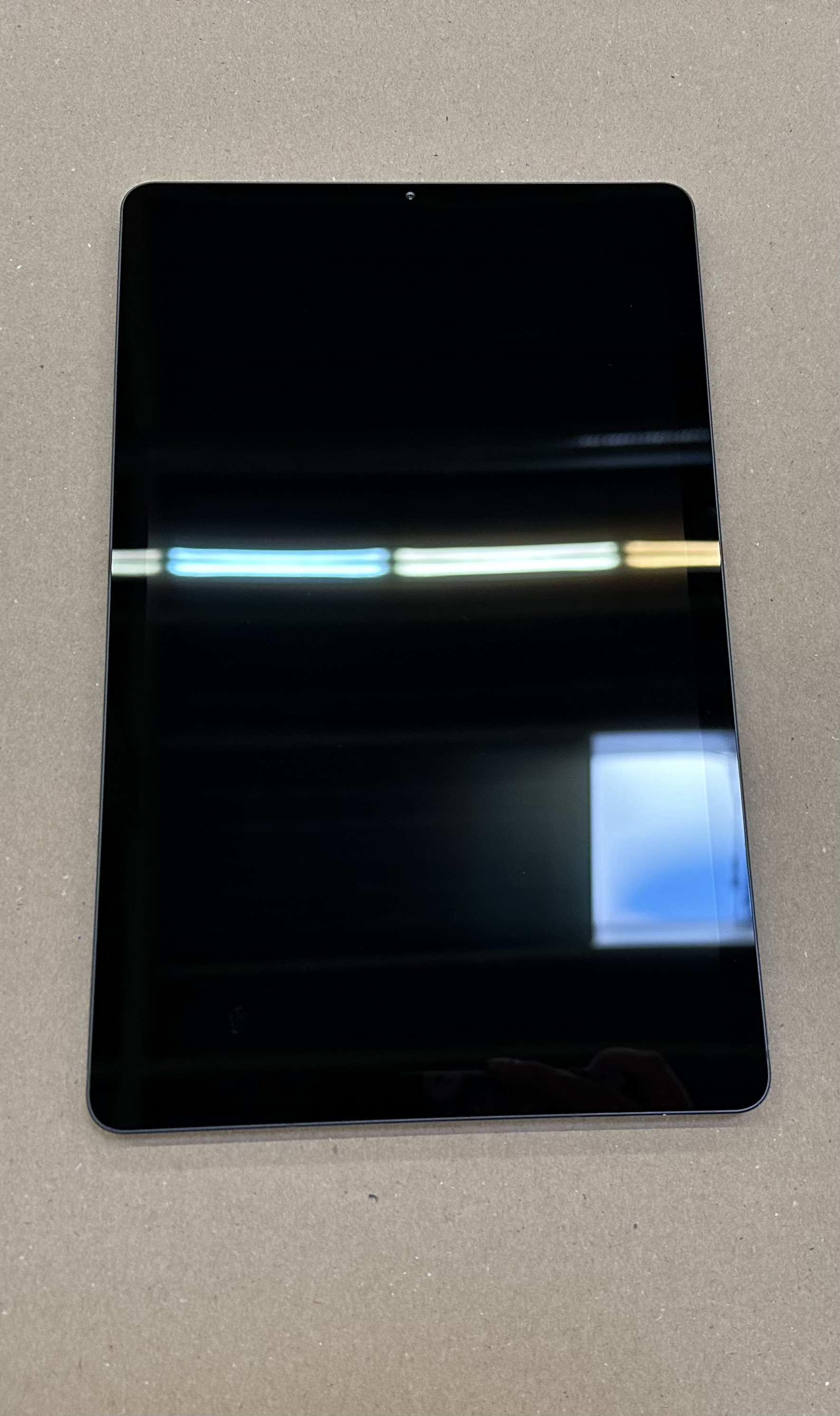 Czarny tablet na szarej powierzchni. Ekran jest ciemny i odbija światło.