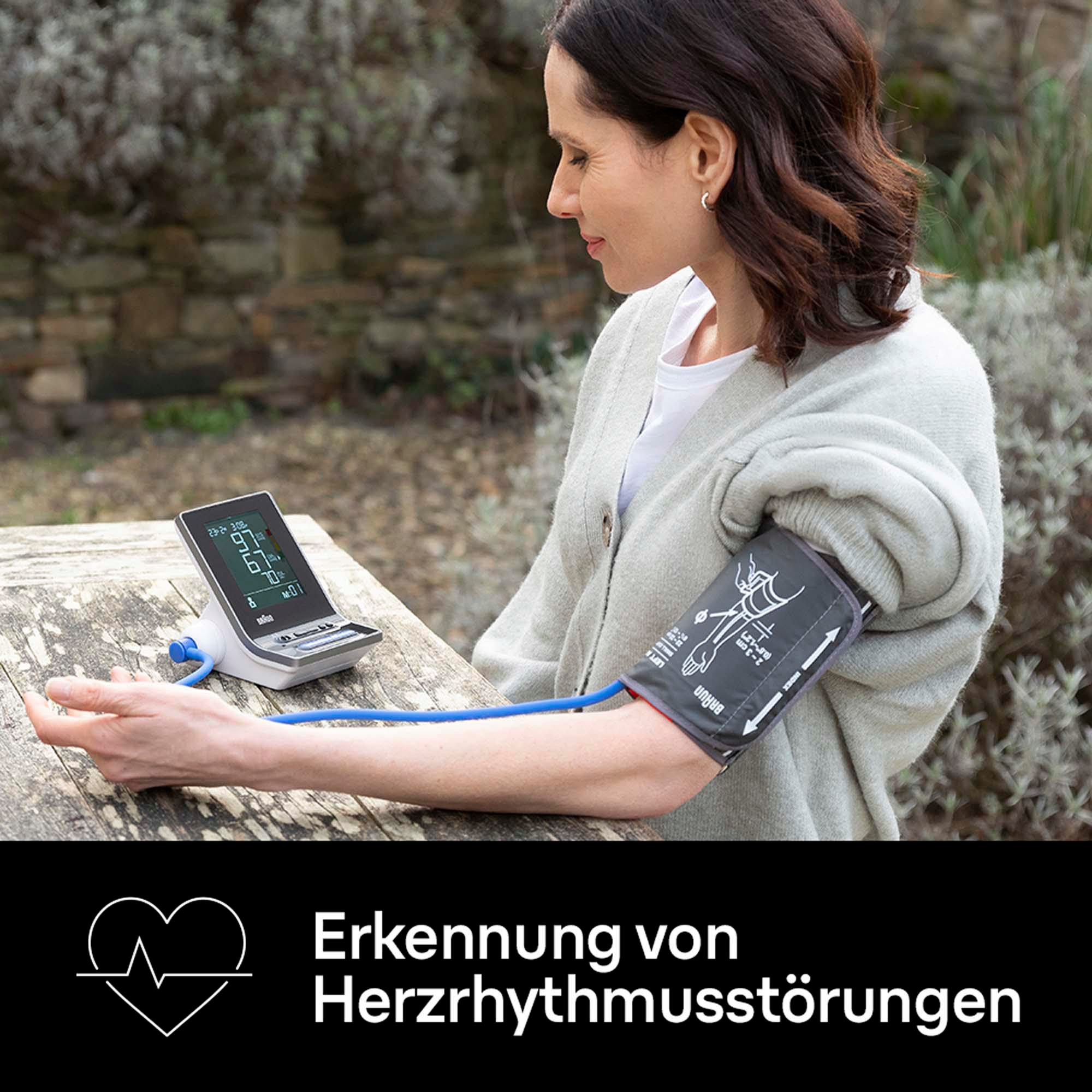 Eine Frau benutzt ein Blutdruckmessgerät, das Display zeigt die Messwerte an. Die Manschette ist am Arm.