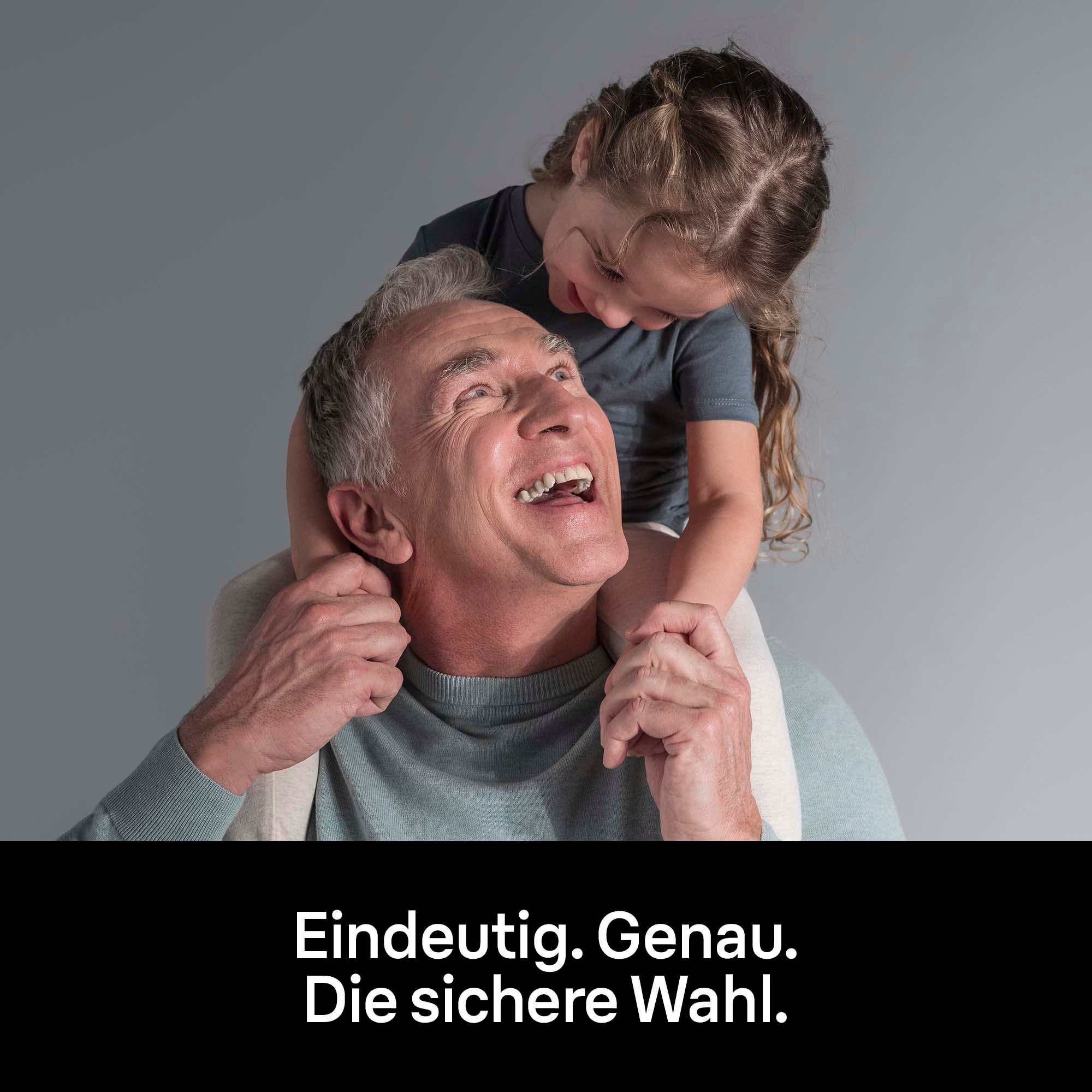 Ein lächelnder Mann trägt ein Mädchen auf seinen Schultern. Sie sind vor grauem Hintergrund.
