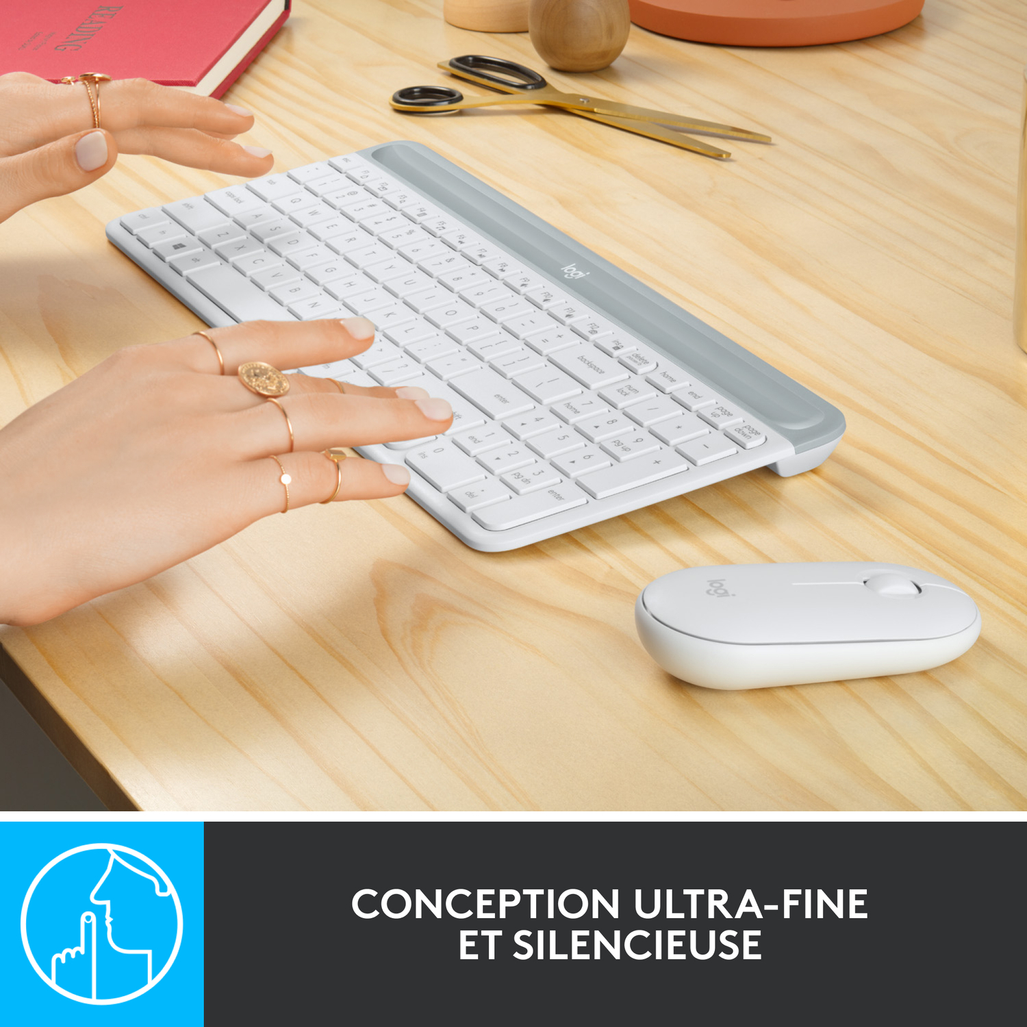 Mains avec des bagues utilisant un clavier et une souris blancs. Une table en bois est visible.