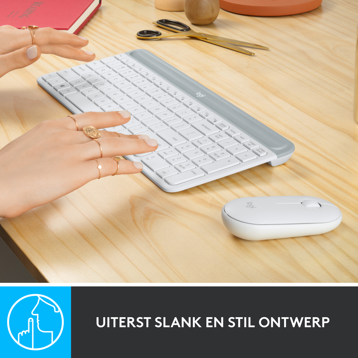 Hands on a wooden desk with a white keyboard and a mouse. Reading material in the background.