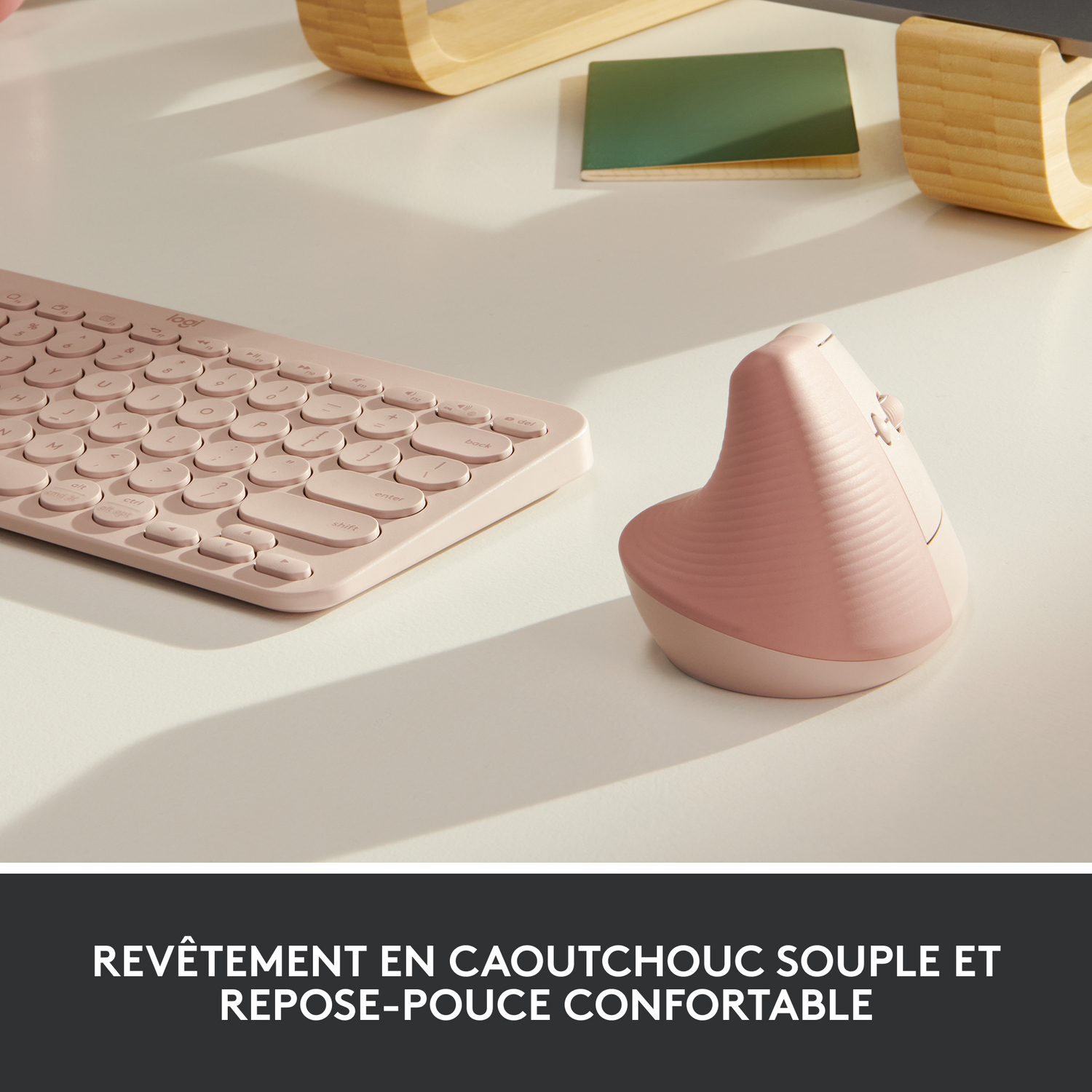 Clavier rose et souris verticale sur bureau blanc, avec objets en bois et verts en arrière-plan.
