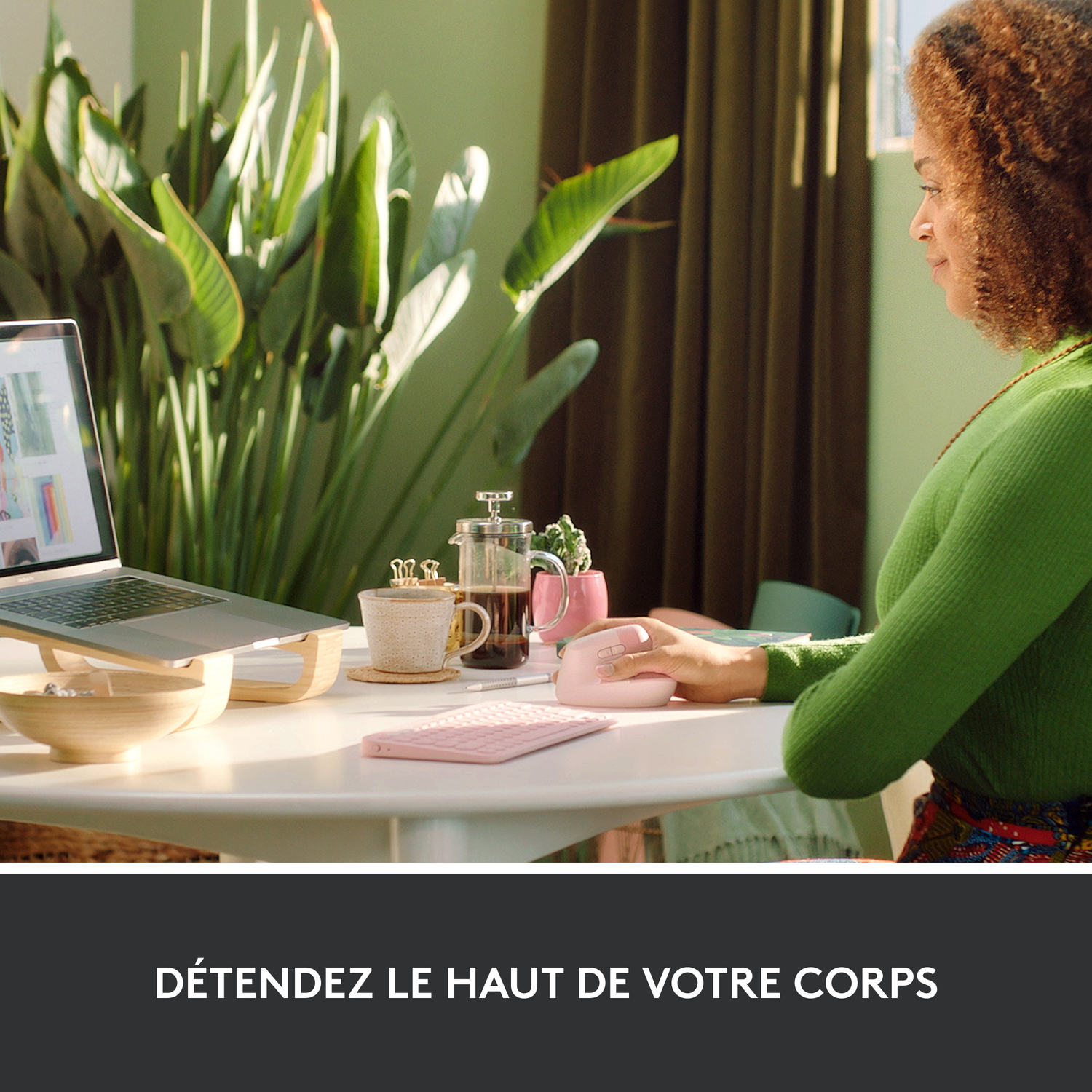 Femme utilisant une souris et un clavier vertical rose sur un bureau, avec un ordinateur portable et du café.