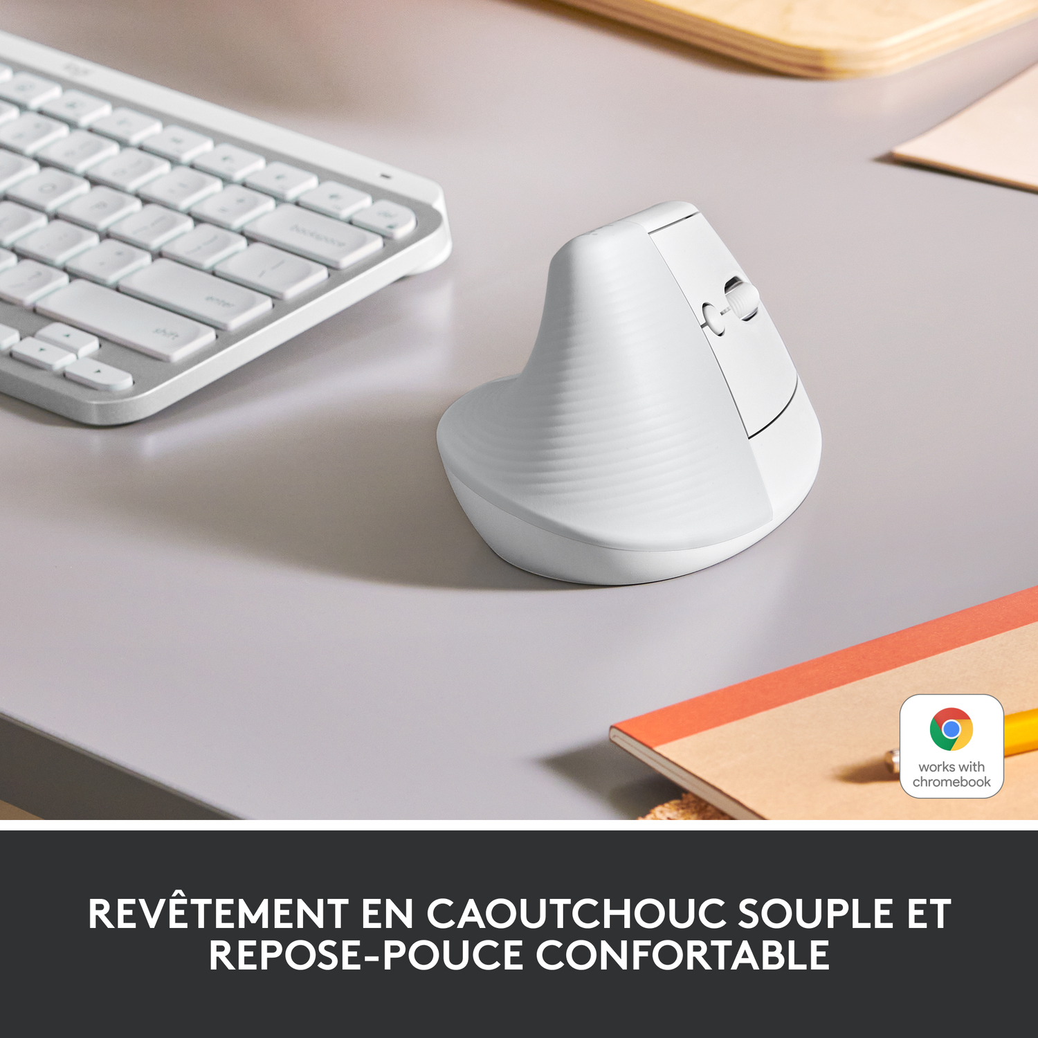 Souris verticale blanche et clavier sur un bureau gris, avec un bloc-notes en arrière-plan.