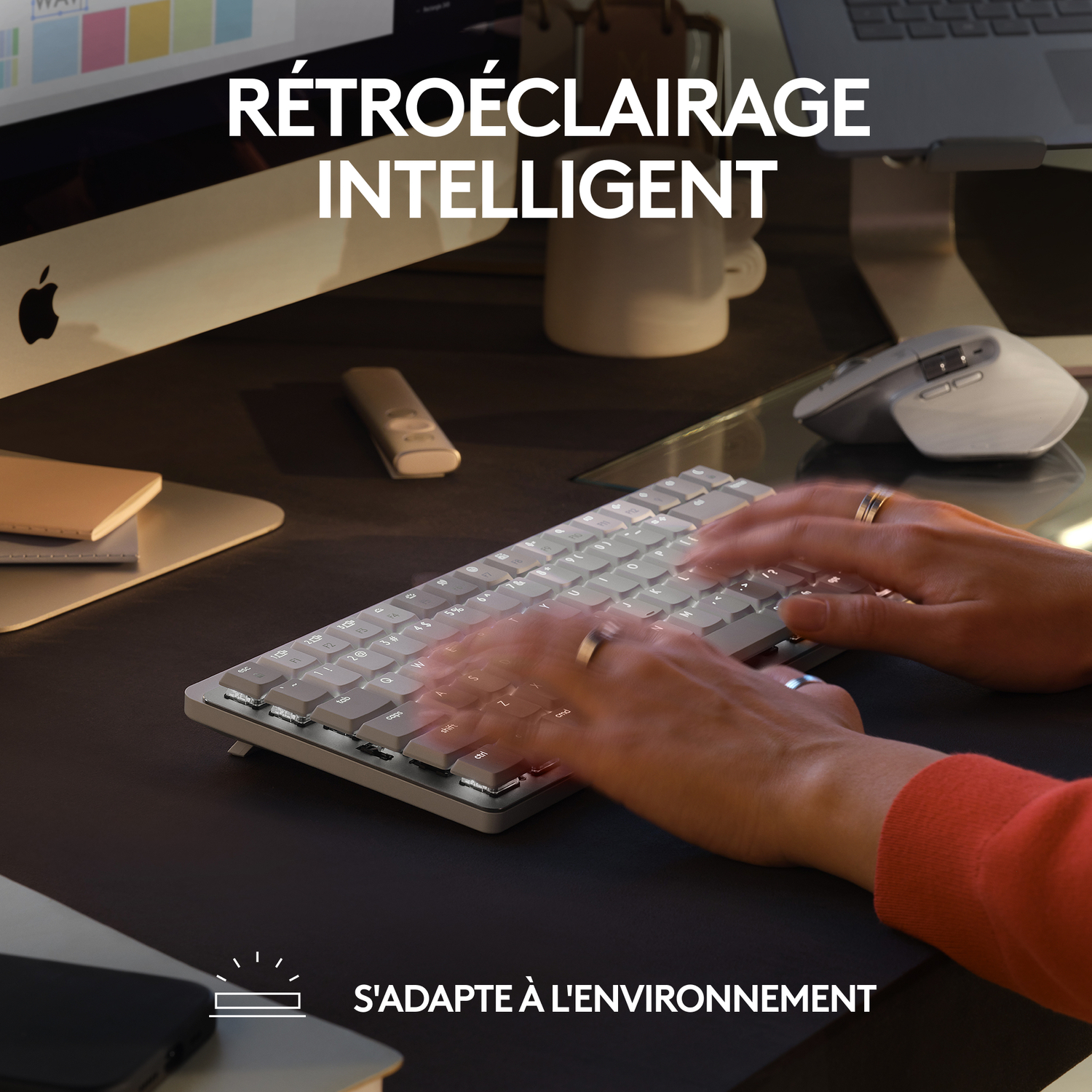 Mains tapant sur un clavier dans une pièce faiblement éclairée. Texte : Rétroéclairage intelligent. S'adapte à l'environnement.