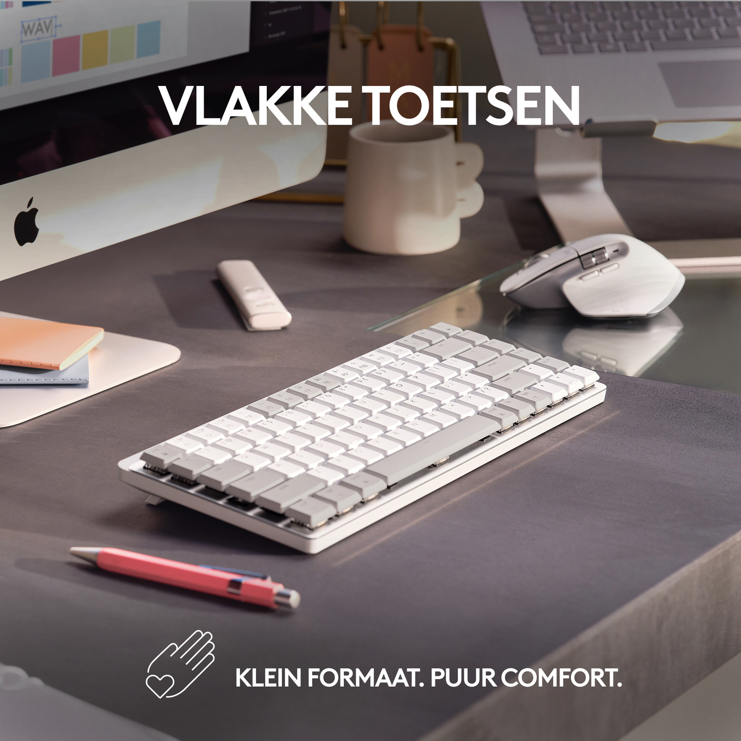 Wit toetsenbord op een grijs bureau. Er is een koffiemok, muis en een rode pen.