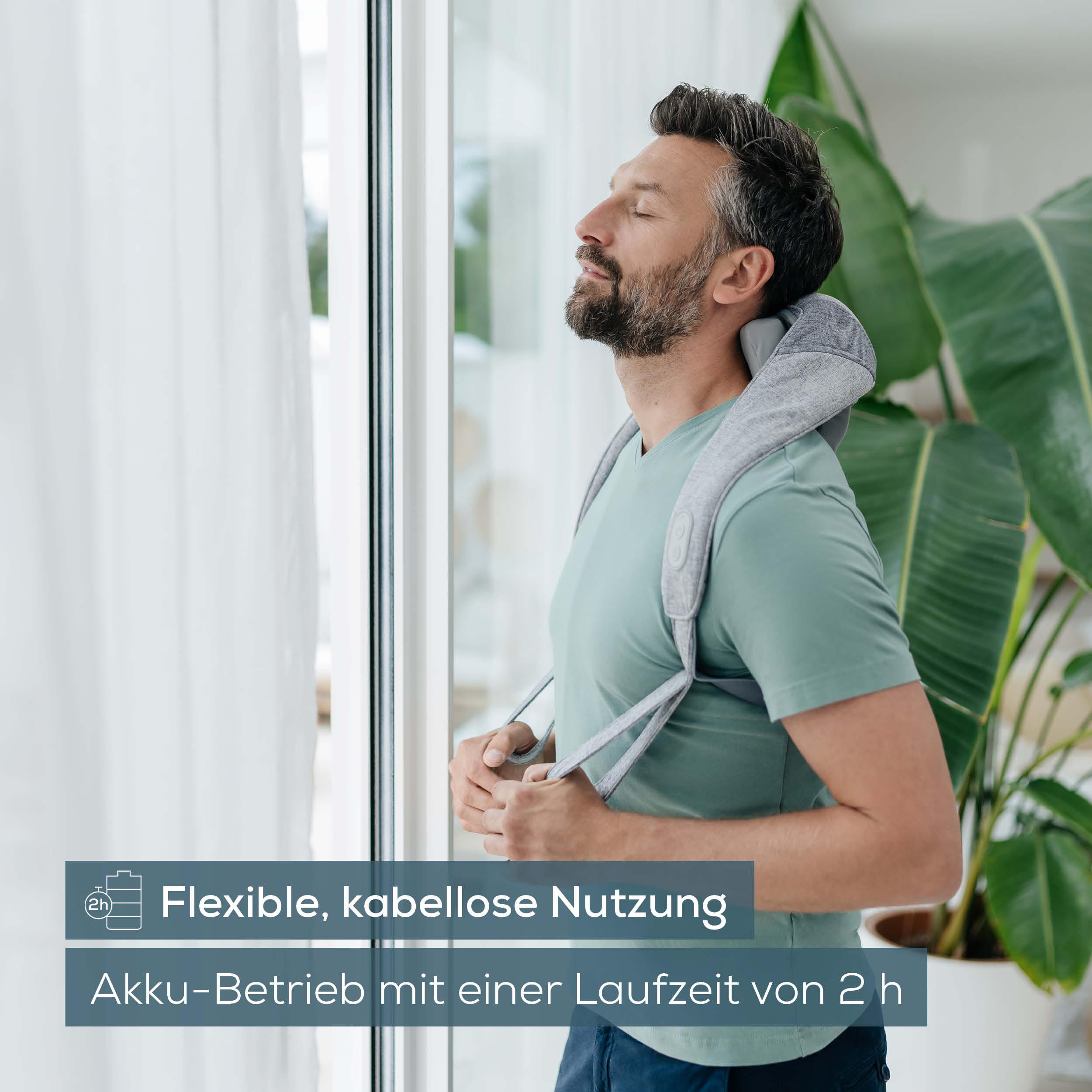 Mann, der ein Nackenmassagegerät benutzt, steht in der Nähe eines Fensters und einer Pflanze.