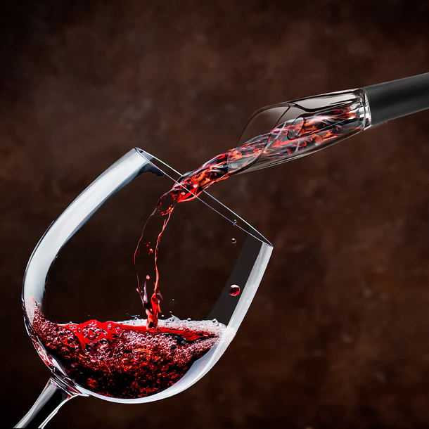Vino tinto vertiéndose en una copa de vino desde un aireador. Fondo oscuro.