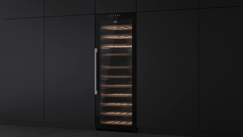 Enfriador de vino negro empotrado con estantes de madera y puerta de cristal, entre armarios negros, manija acero inoxidable.