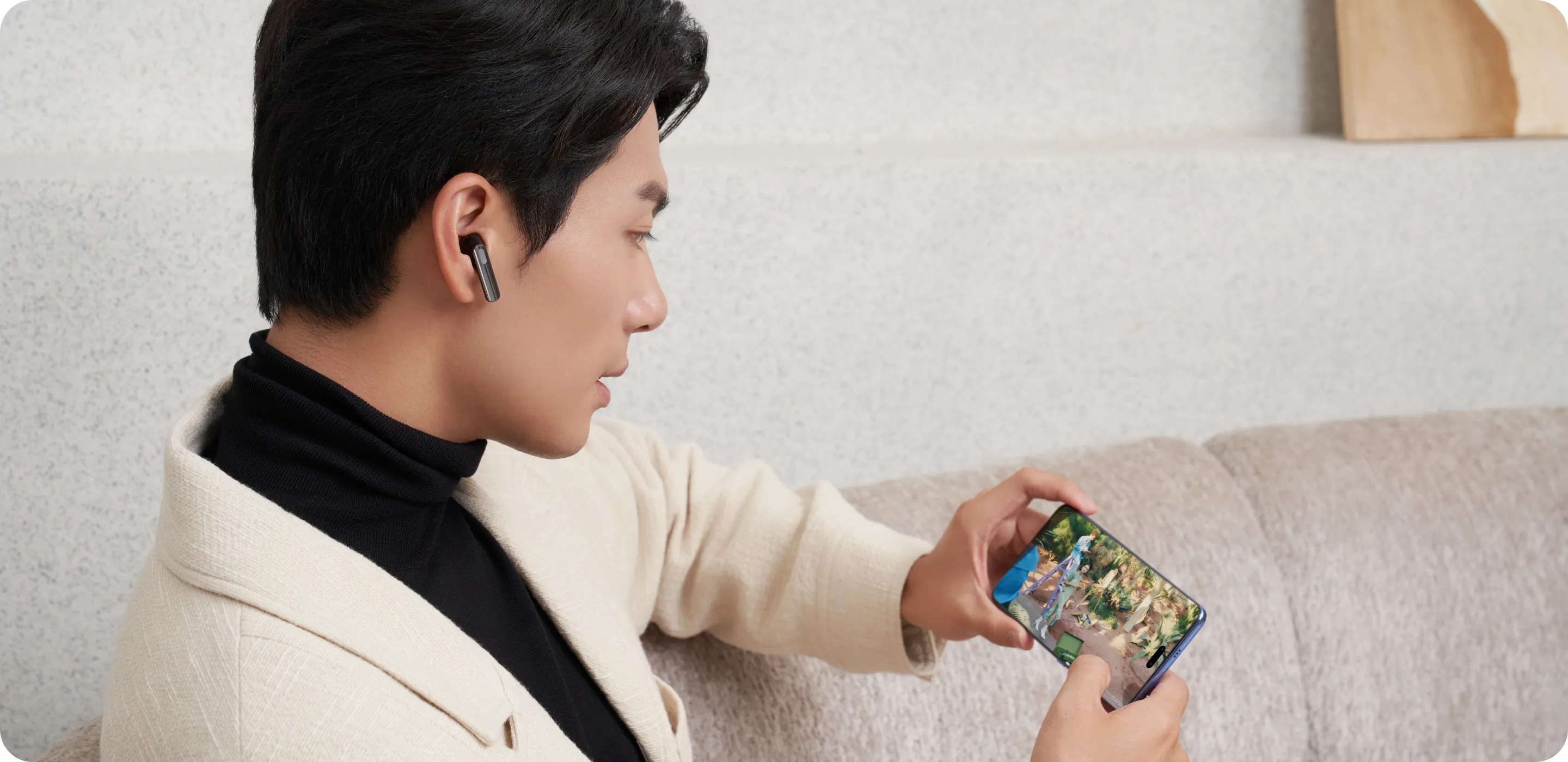 Mężczyzna ogląda wideo na telefonie, mając na uszach słuchawki. Słuchawki mają złoty akcent.