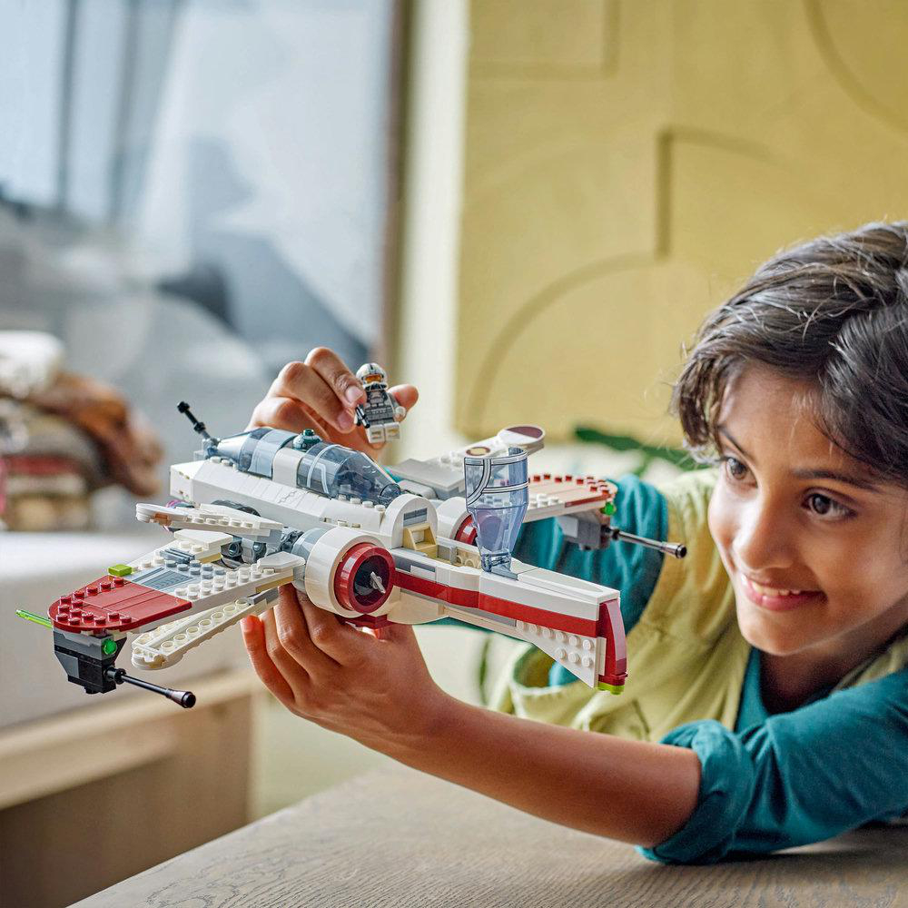Ein Kind hält einen Lego Star Wars X-Wing-Jäger. Er ist weiß mit roten Akzenten, und eine Minifigur ist oben drauf.