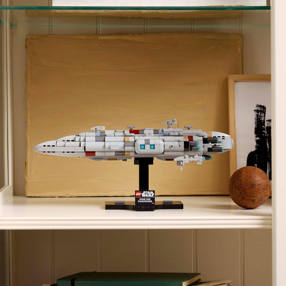 Ein weiß-graues LEGO Star Wars Schiffsmodell auf einem Regal. Ein gerahmtes Bild und eine braune Kugel im Hintergrund.