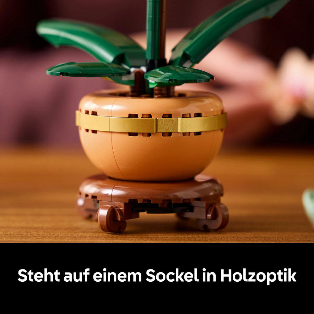 Orchideen-Pflanze-Lego-Set auf braunem Ständer. Der Topf ist beige mit Goldband, grünen Blättern, unscharfer HG.