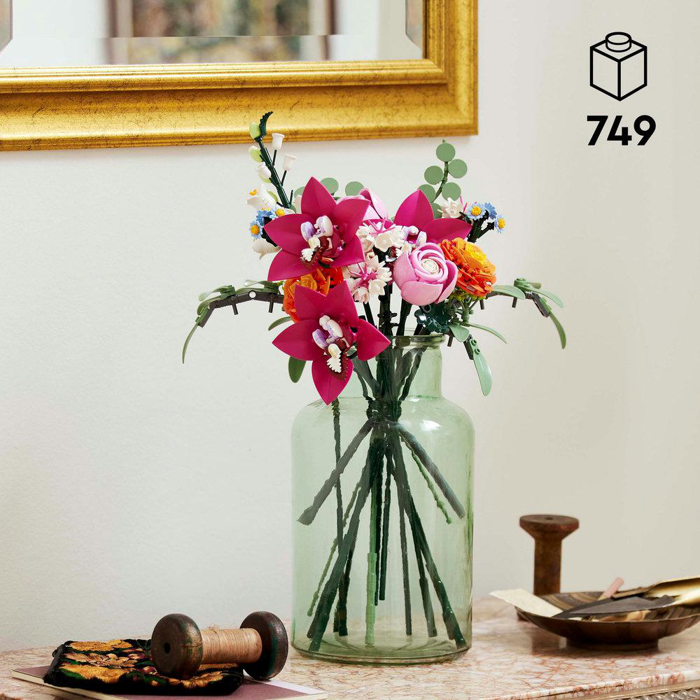 Eine Vase mit bunten Blumen auf einem Tisch. Eine Holzspule und ein Dekoartikel liegen daneben.